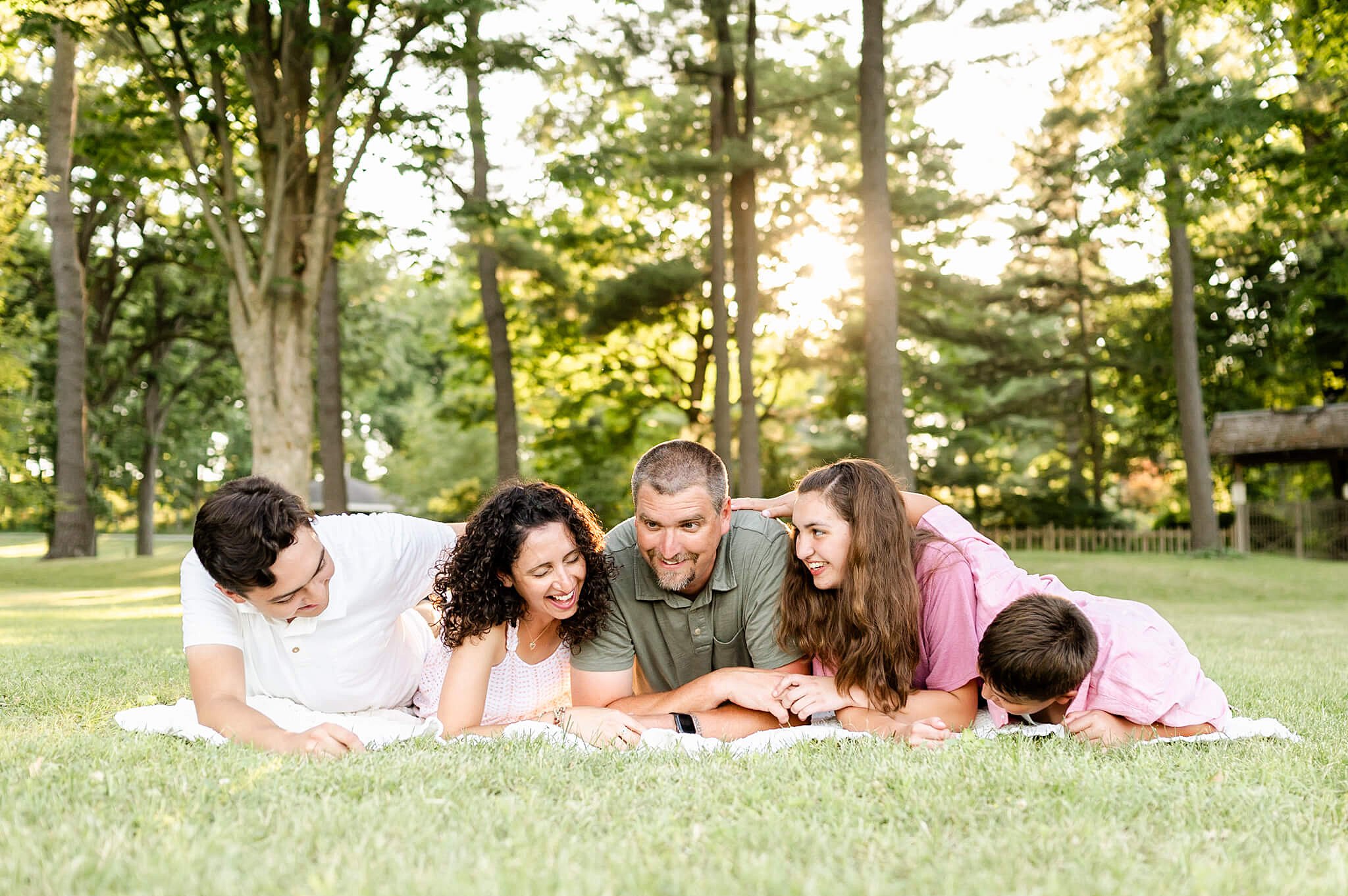 family of 5 laughing on a picnic blanket in a park