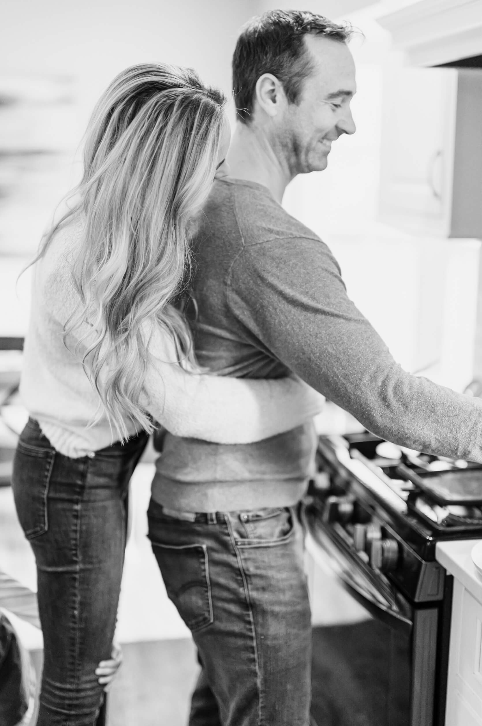 woman hugging a man from behind as he cooks in the kitchen