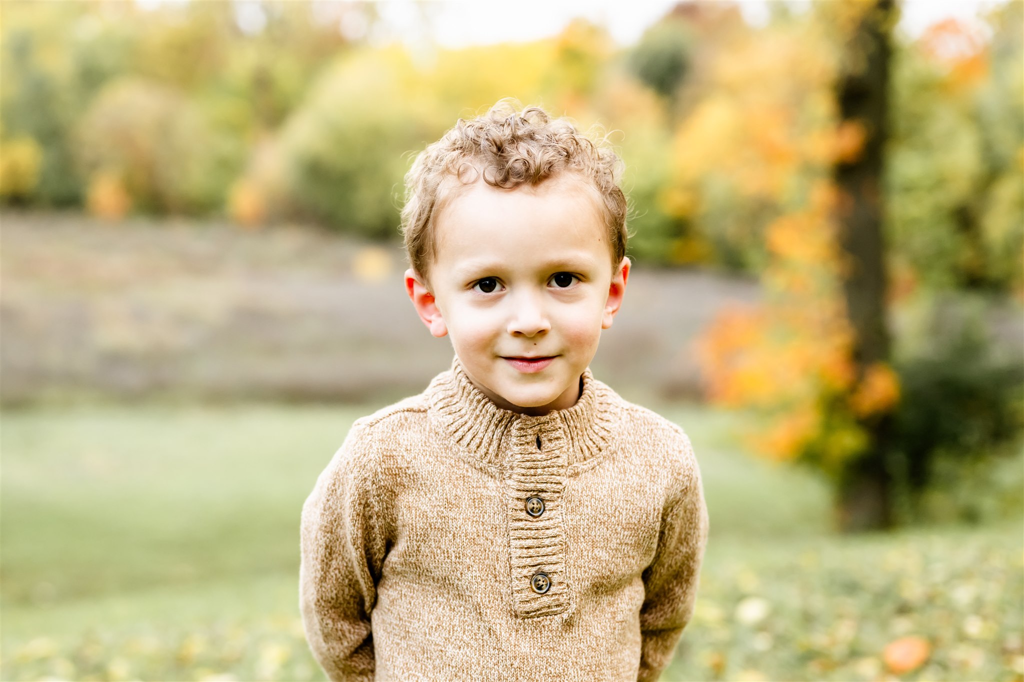 A young boy in a brown sweater stands in a park in fall with hands behind him before a Brookfield Zoo Birthday Party
