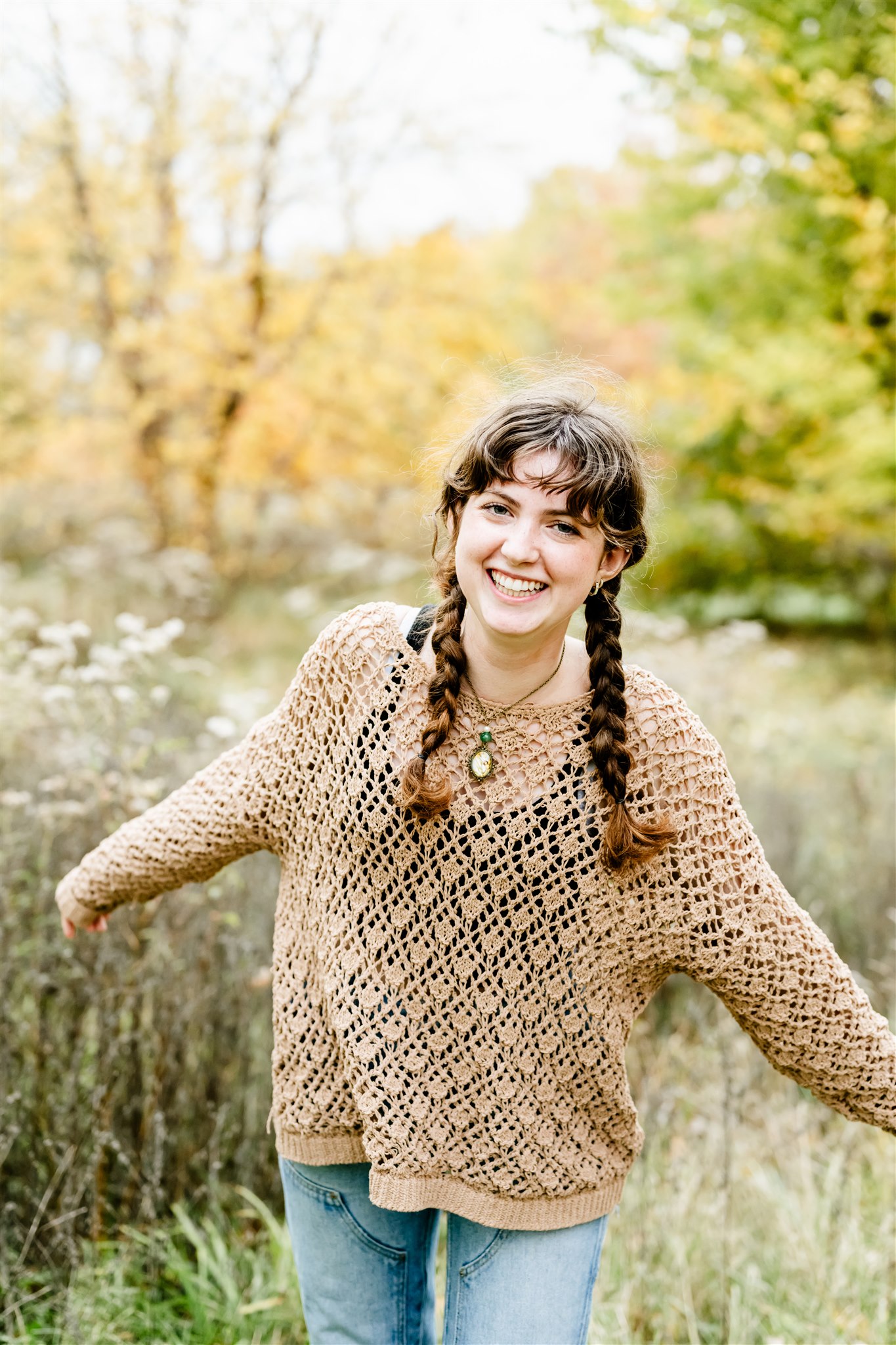 A high school senior in jeans and a lace sweater laughs while walking through a field of tall grasses thanks to Catholic High Schools Chicago Suburbs