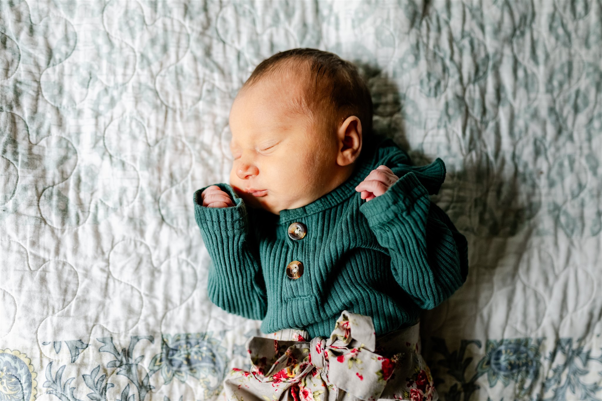 A newborn baby sleeps in a teal sweater on a bed thanks to Home Daycare Chicago
