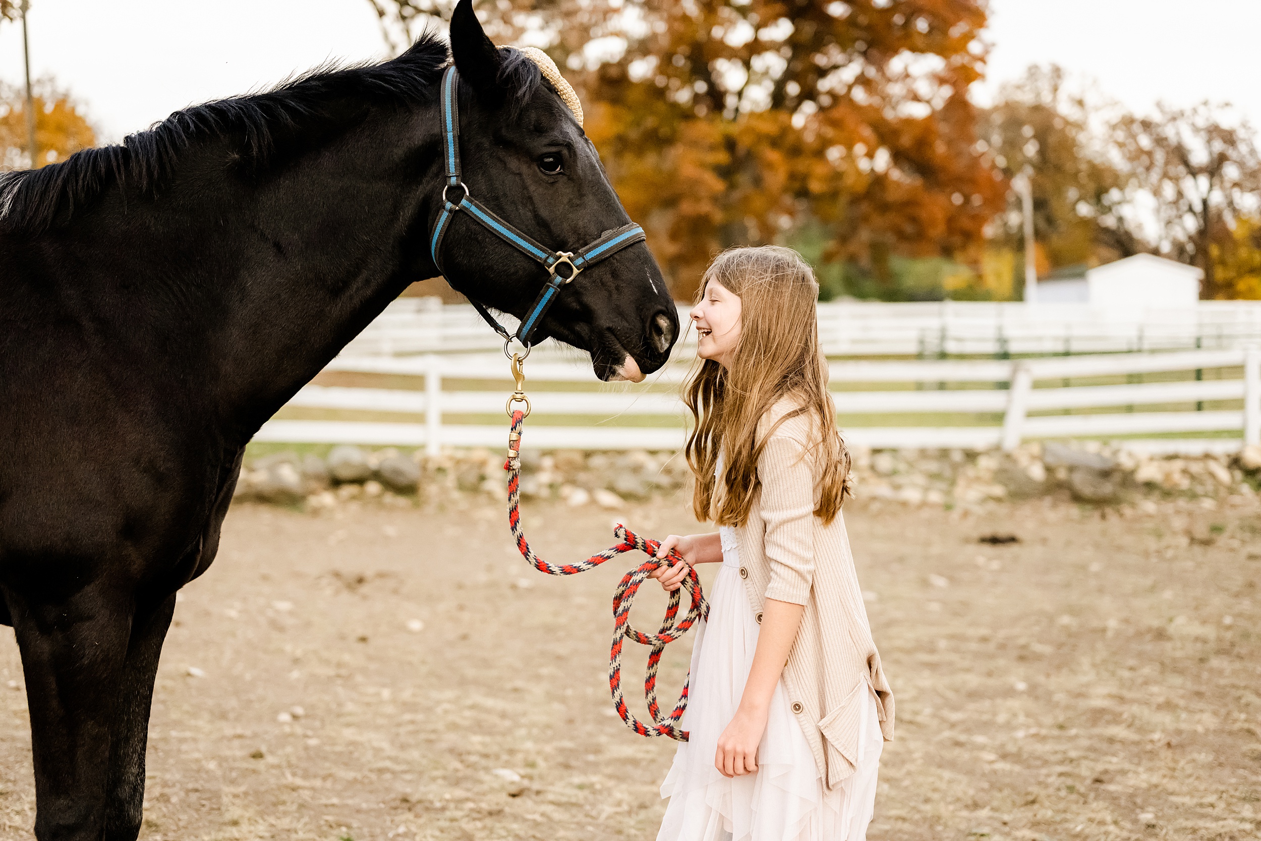 A young girl laughs while walking her horse in a pasture