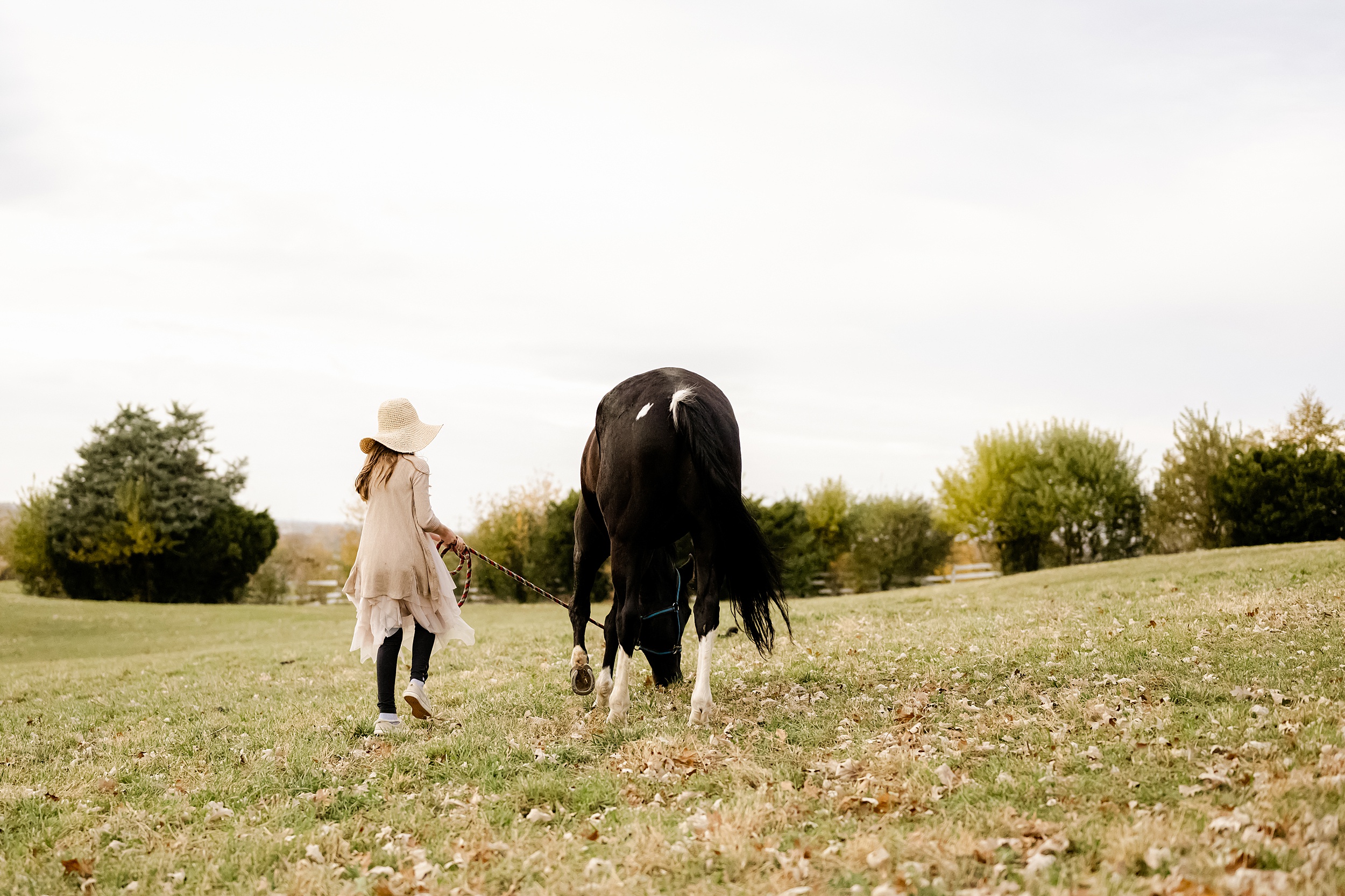 A young girl walks her horse through a pasture in a large hat during horseback riding for kids chicago