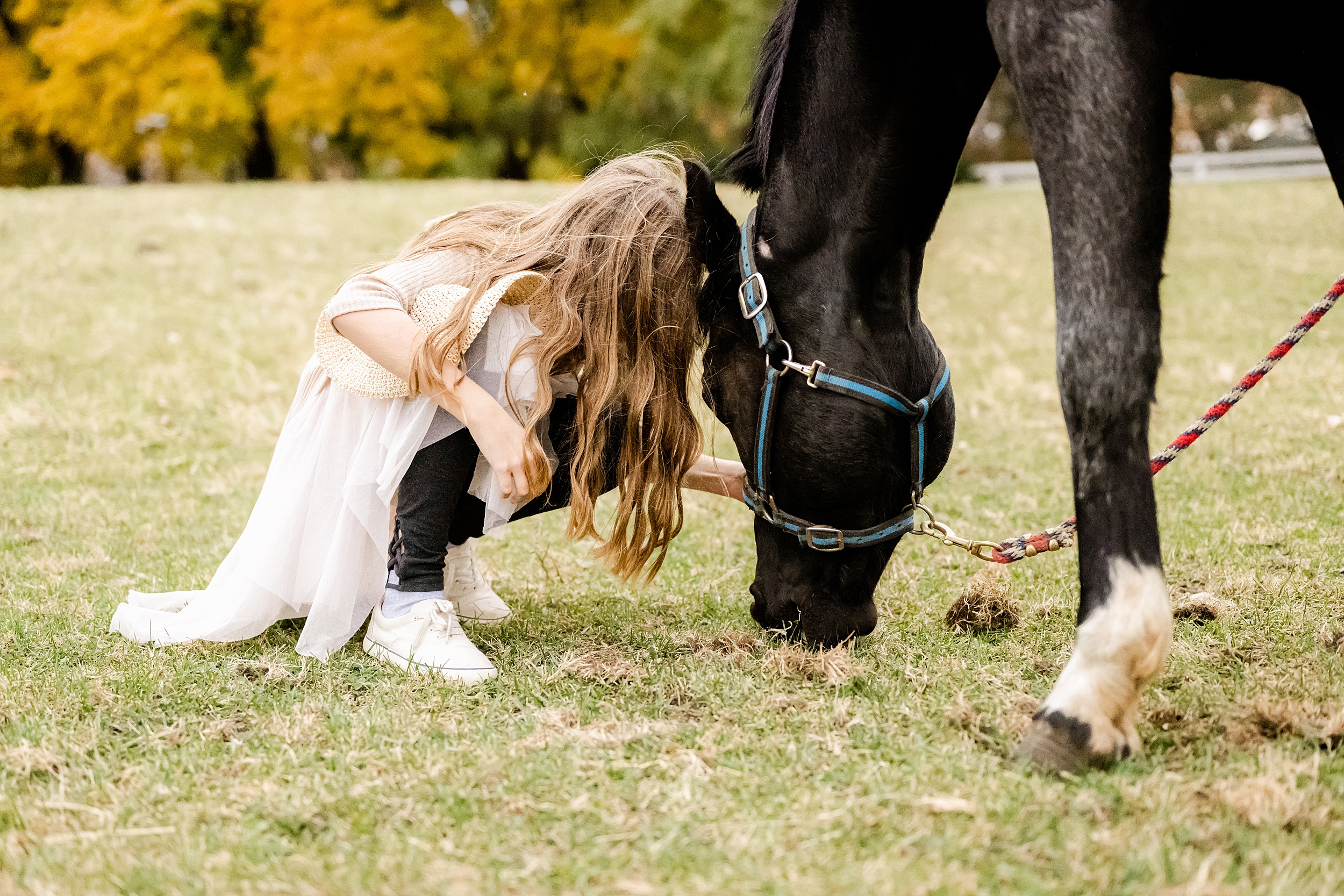 A girl squats down with her horse as it grazes during horseback riding for kids chicago
