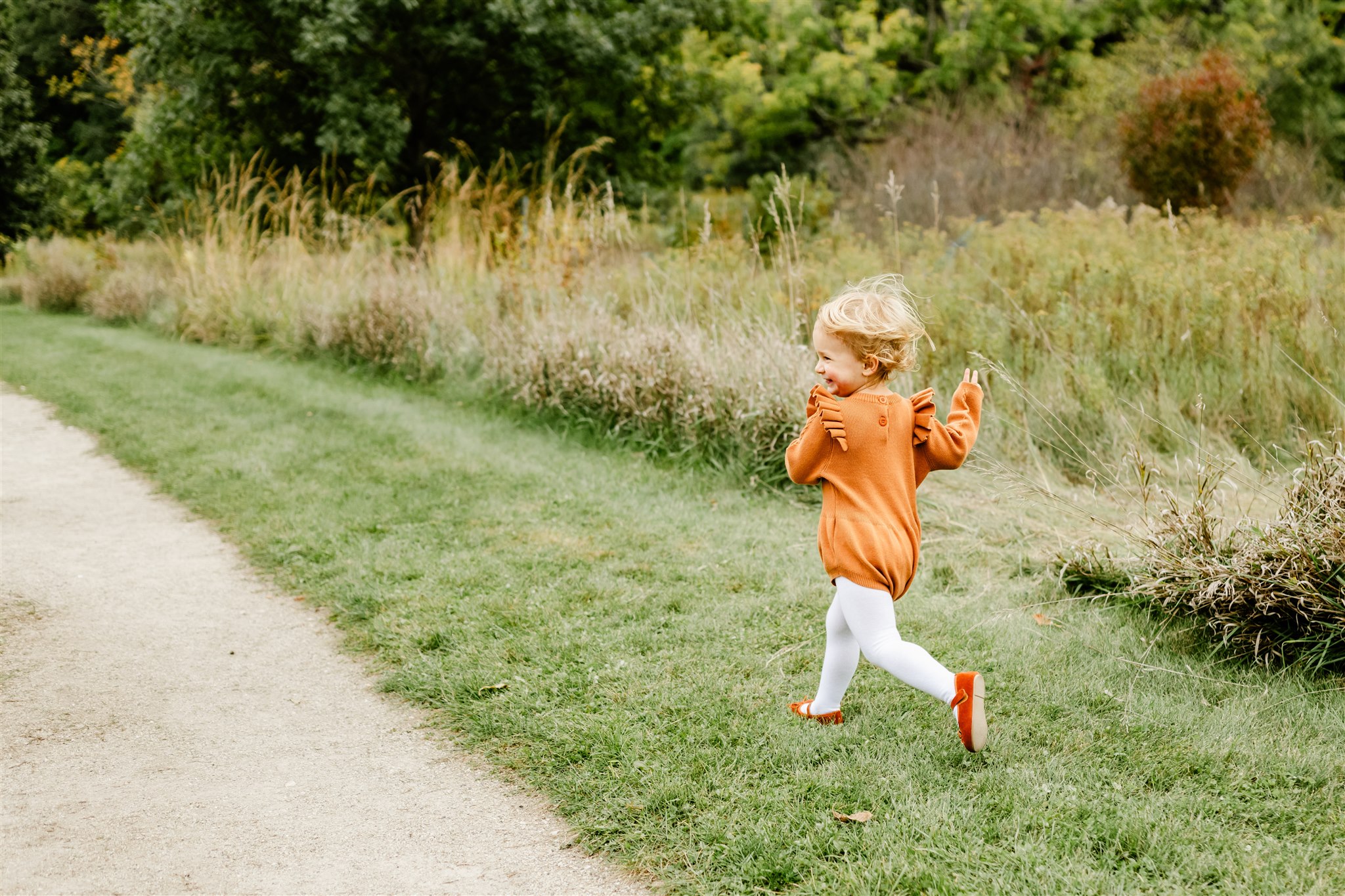 A young girl in an orange dress runs through a park trail while laughing before visiting Kid Friendly Restaurants Naperville