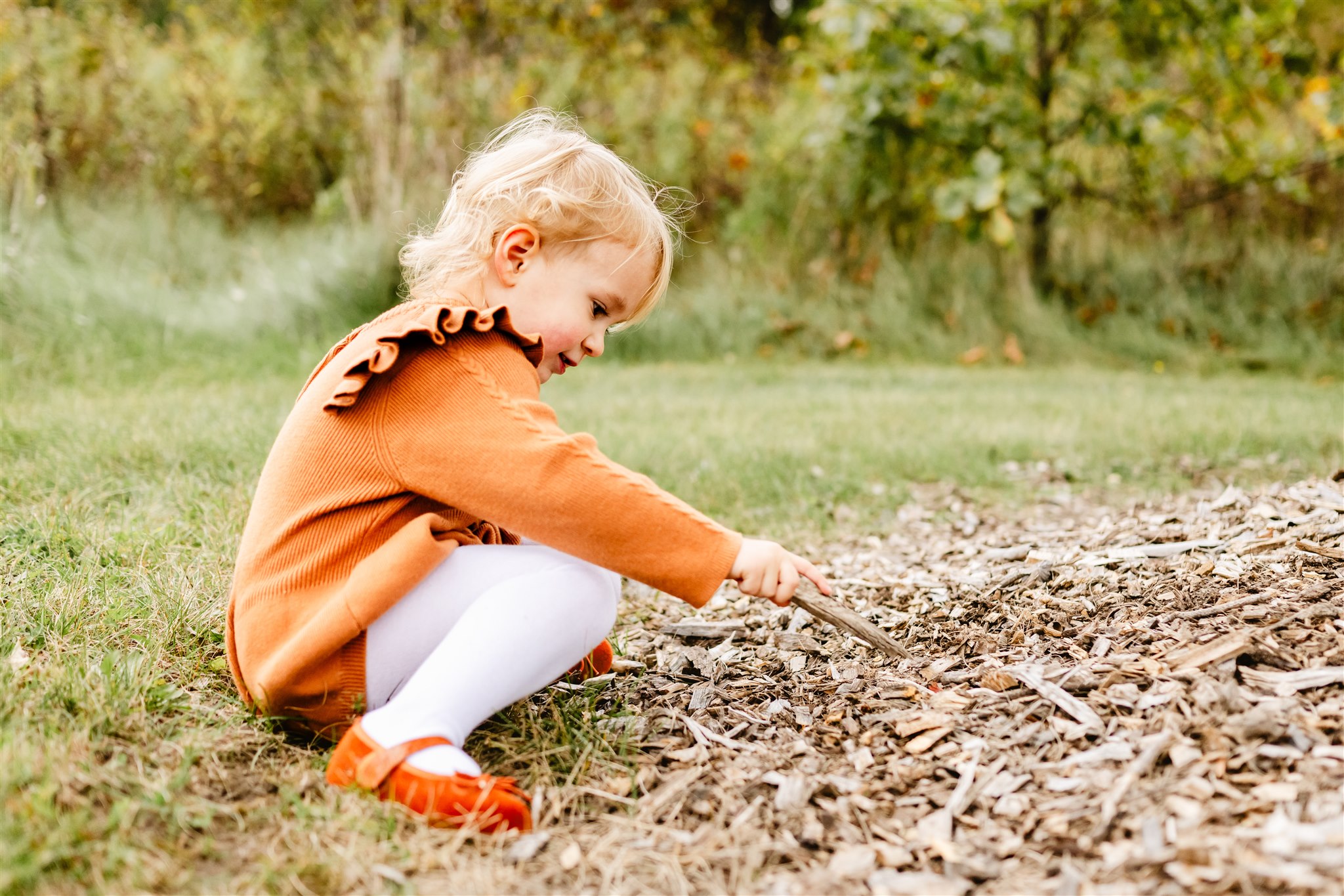 A young girl in an orange dress plays with sticks in a park on the ground before visiting Kid Friendly Restaurants Naperville