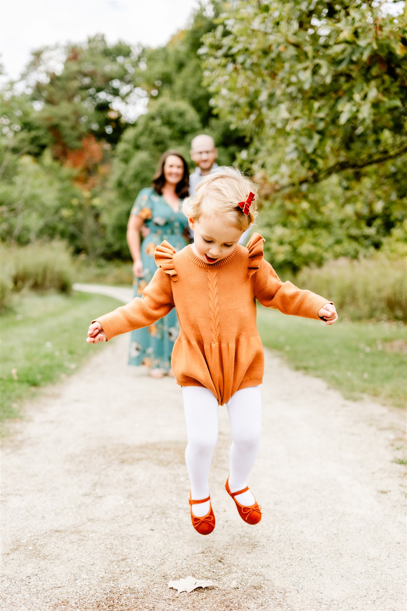 A toddler girl in an orange dress jump in a park path