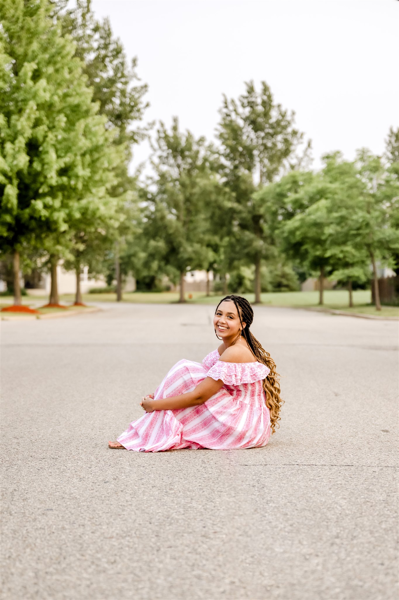 A high school senior in a striped pink dress sits in a road before shopping for Prom Dresses Chicago