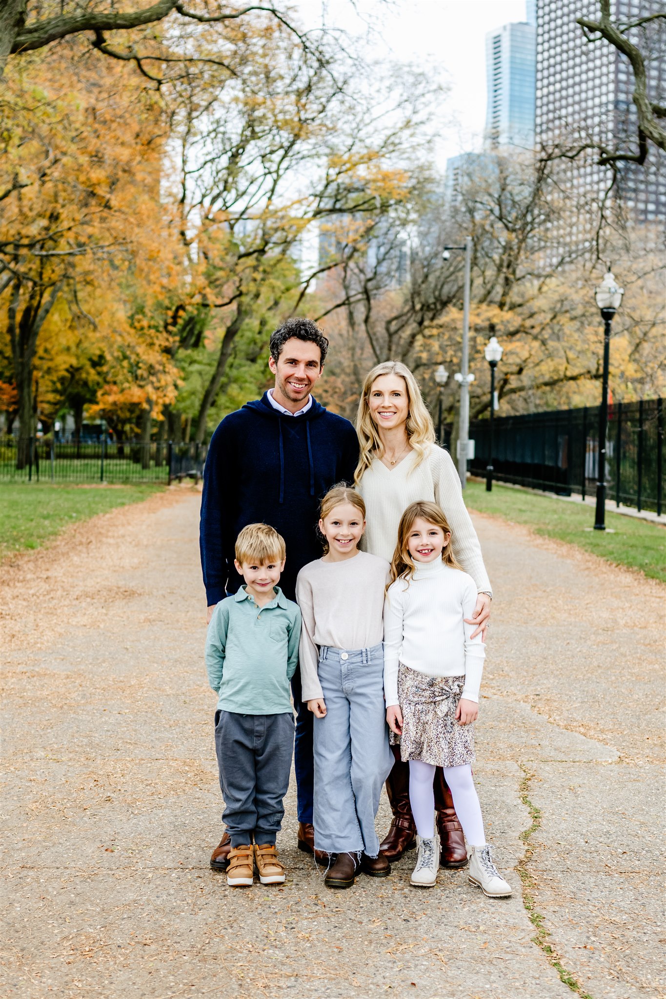 A mom and dad stand in a metropolitan park path behind their three young children