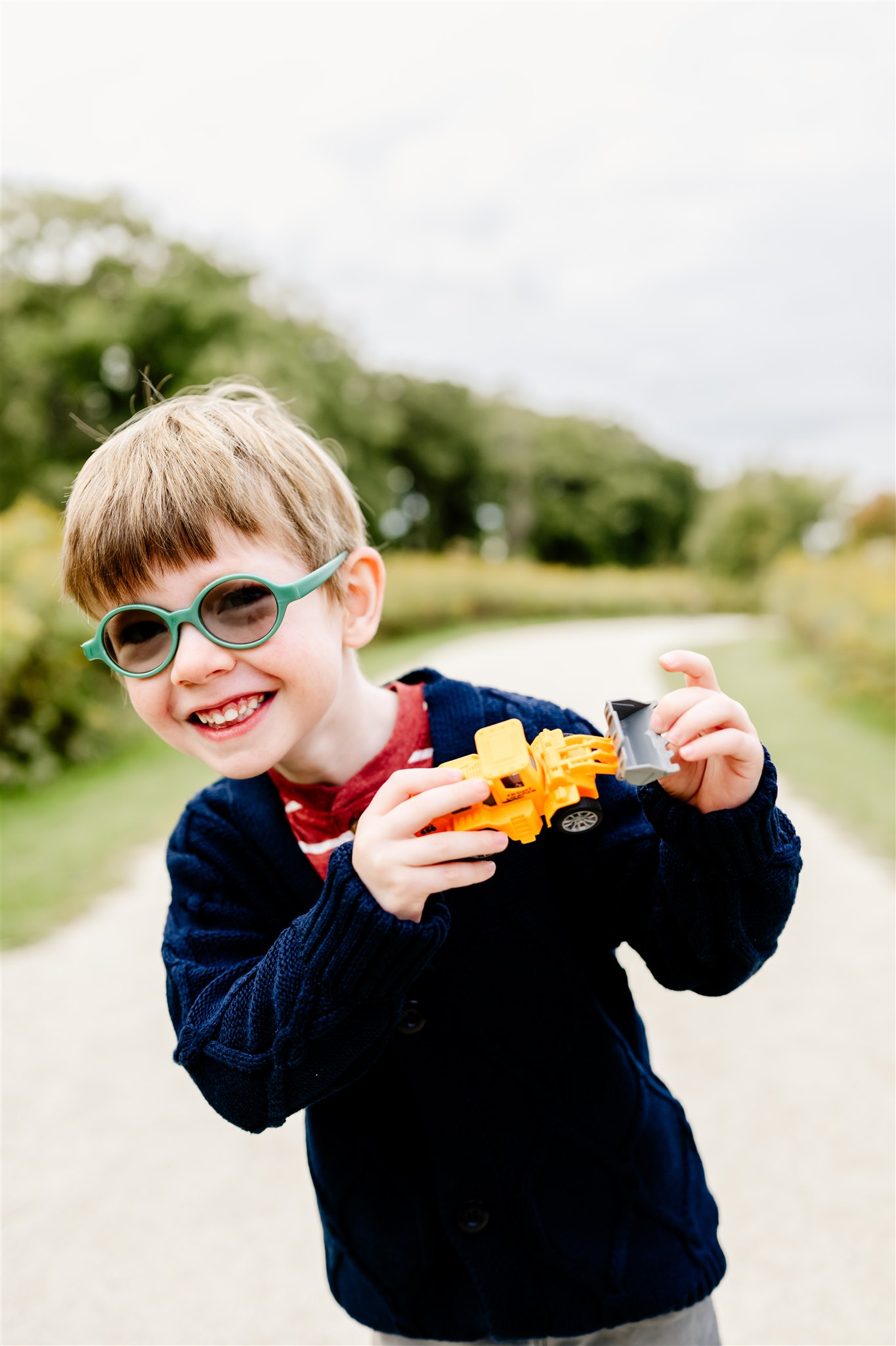 A young boy in a blue sweater and glasses plays with a toy front end loader in a park path thanks to STEM Chicago