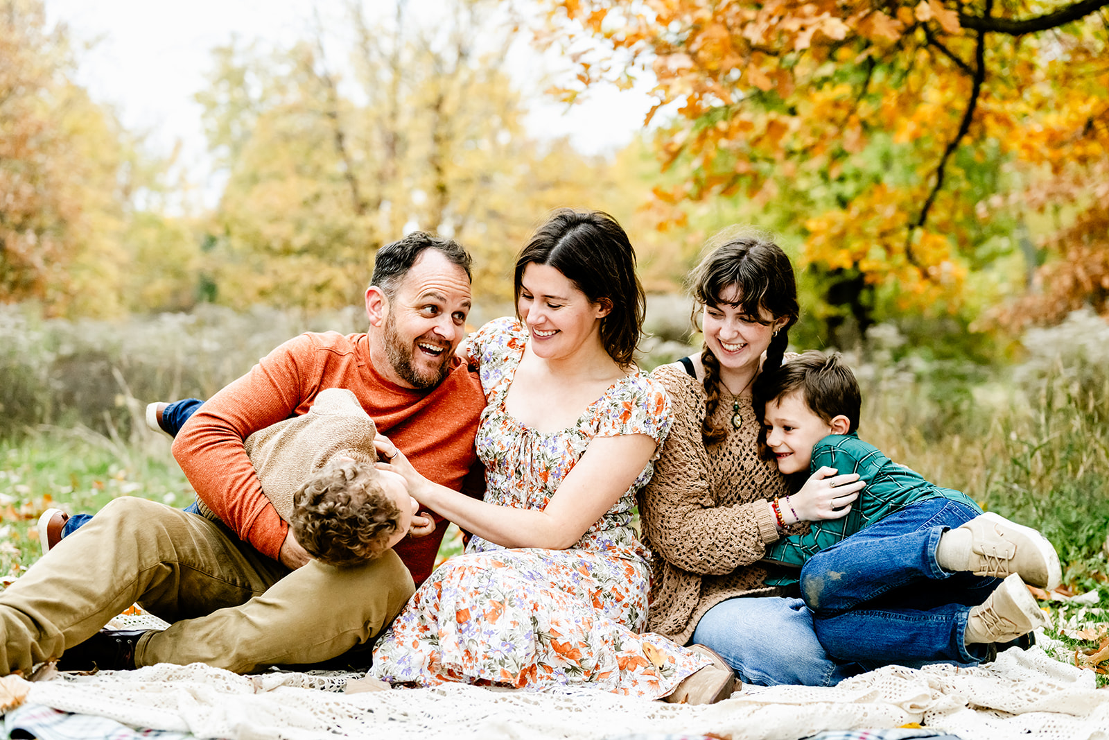A happy family of 5 play in a park lawn on a blanket with big smiles