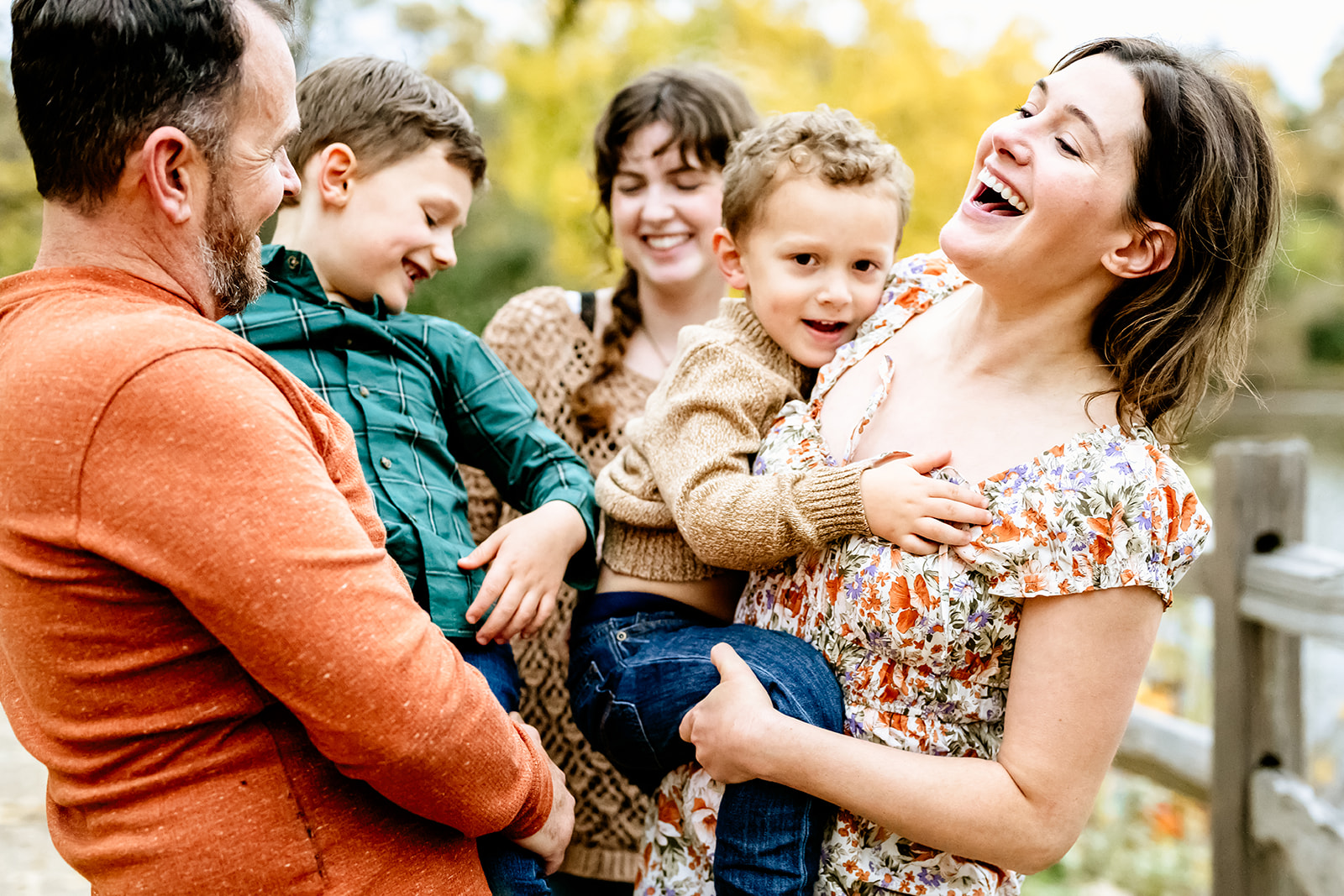 Happy mom and dad play with their toddlers in their arms in a park trail with teen laughing behind them after some christian summer camps in Illinois