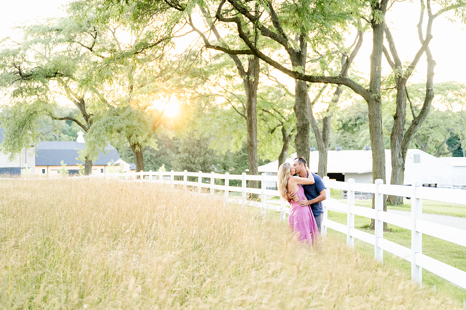 A happy engaged couple kiss on the edge of a pasture at sunset before visiting Comedy Vault Batavia