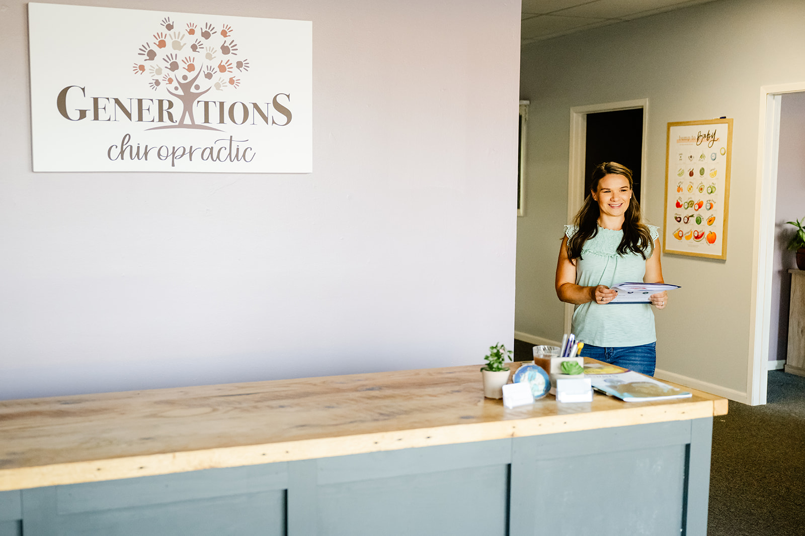 A woman in a green blouse walks behind the front desk of Generations Chiropractic