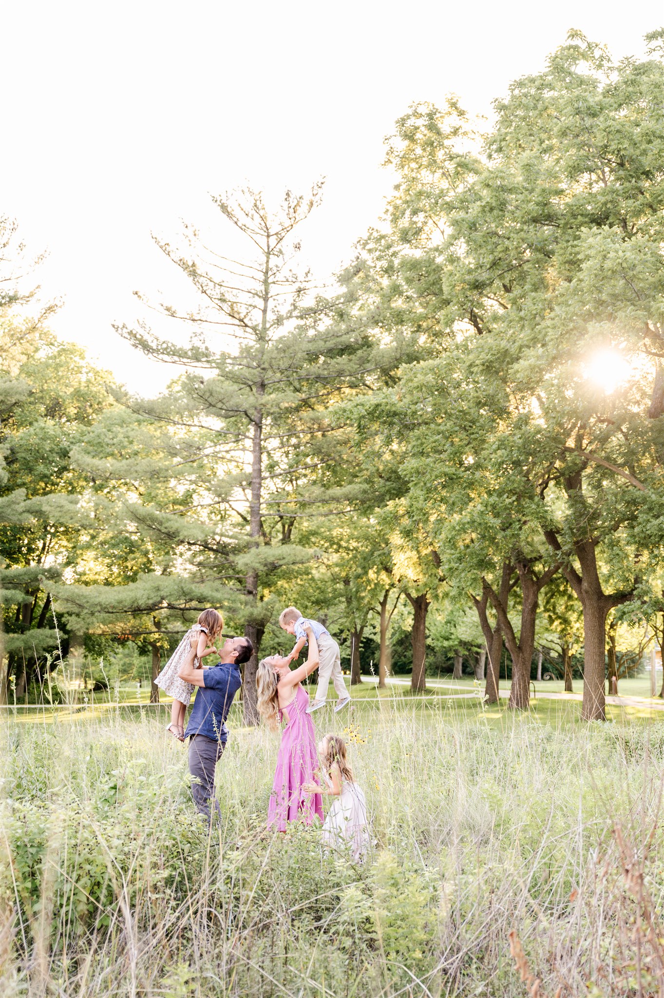 Happy mom and dad lift their toddlers above their heads in a park at sunset after some kids swim lessons in Chicago