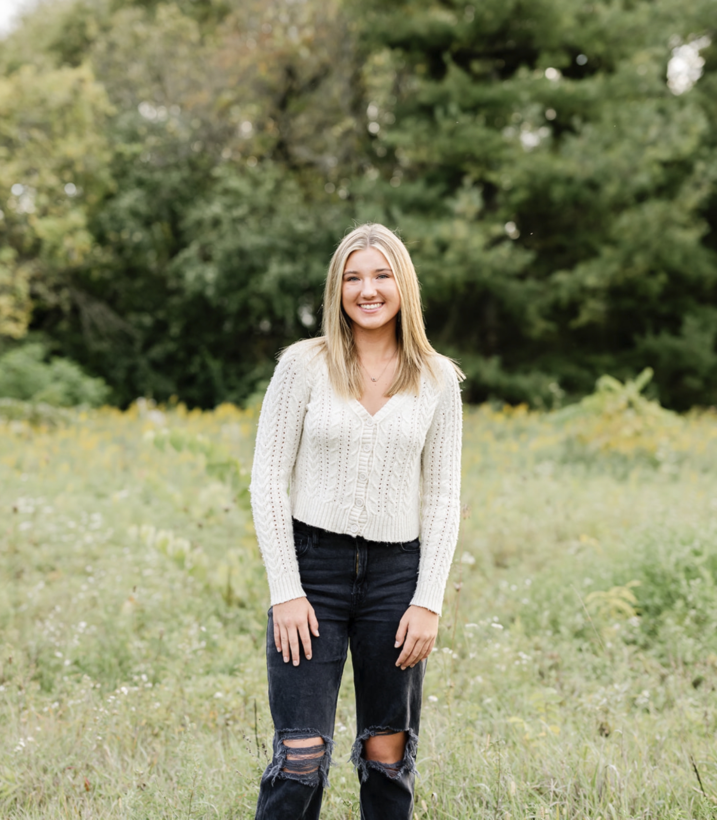 A teenager in black ripped jeans and white sweater walks in a park meadow