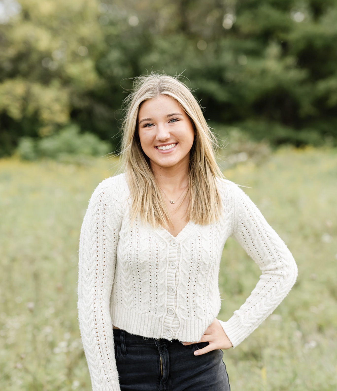 A high school senior stands in a meadow in a white sweater with a hand on her hip after visiting boutiques in Chicago