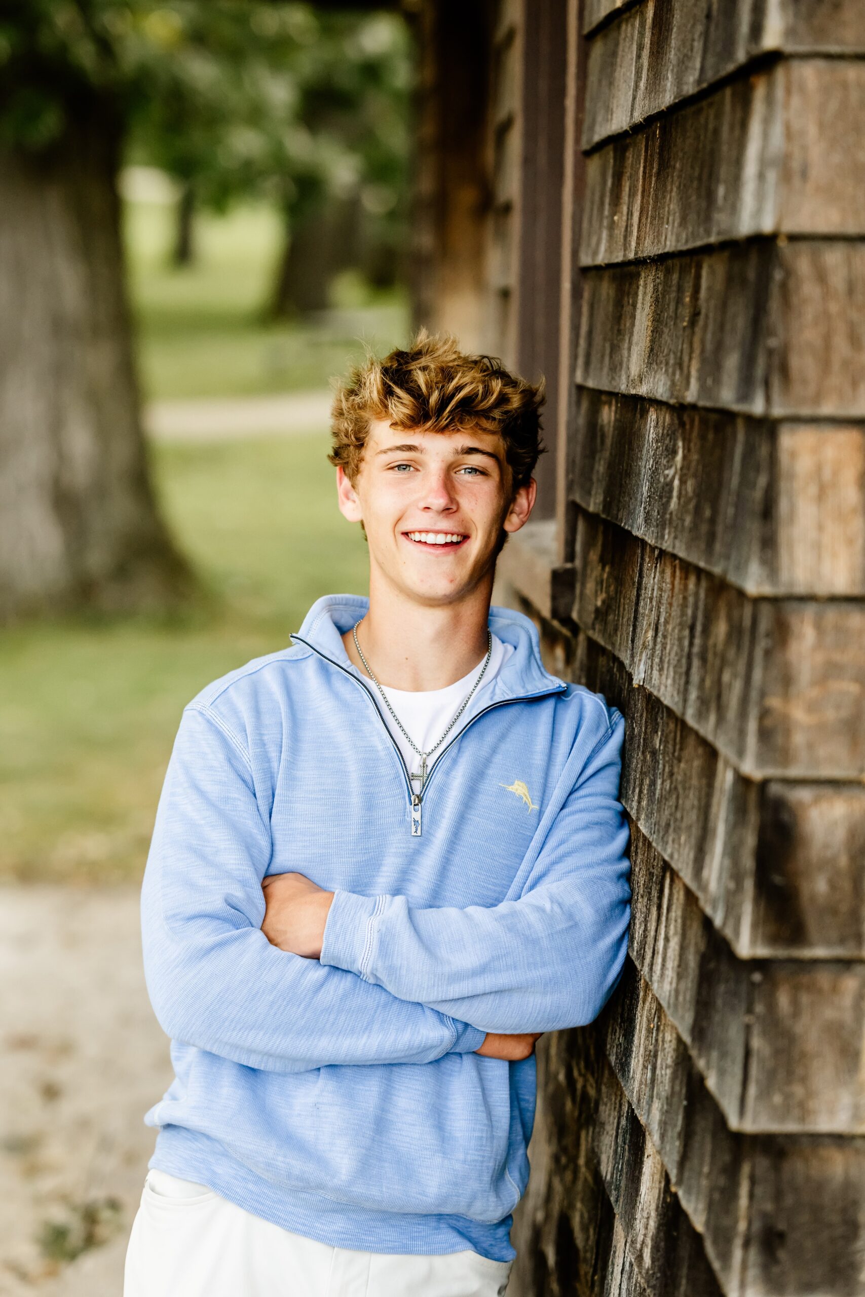 A teenager leans on a rustic building in blue and white with arms crossed