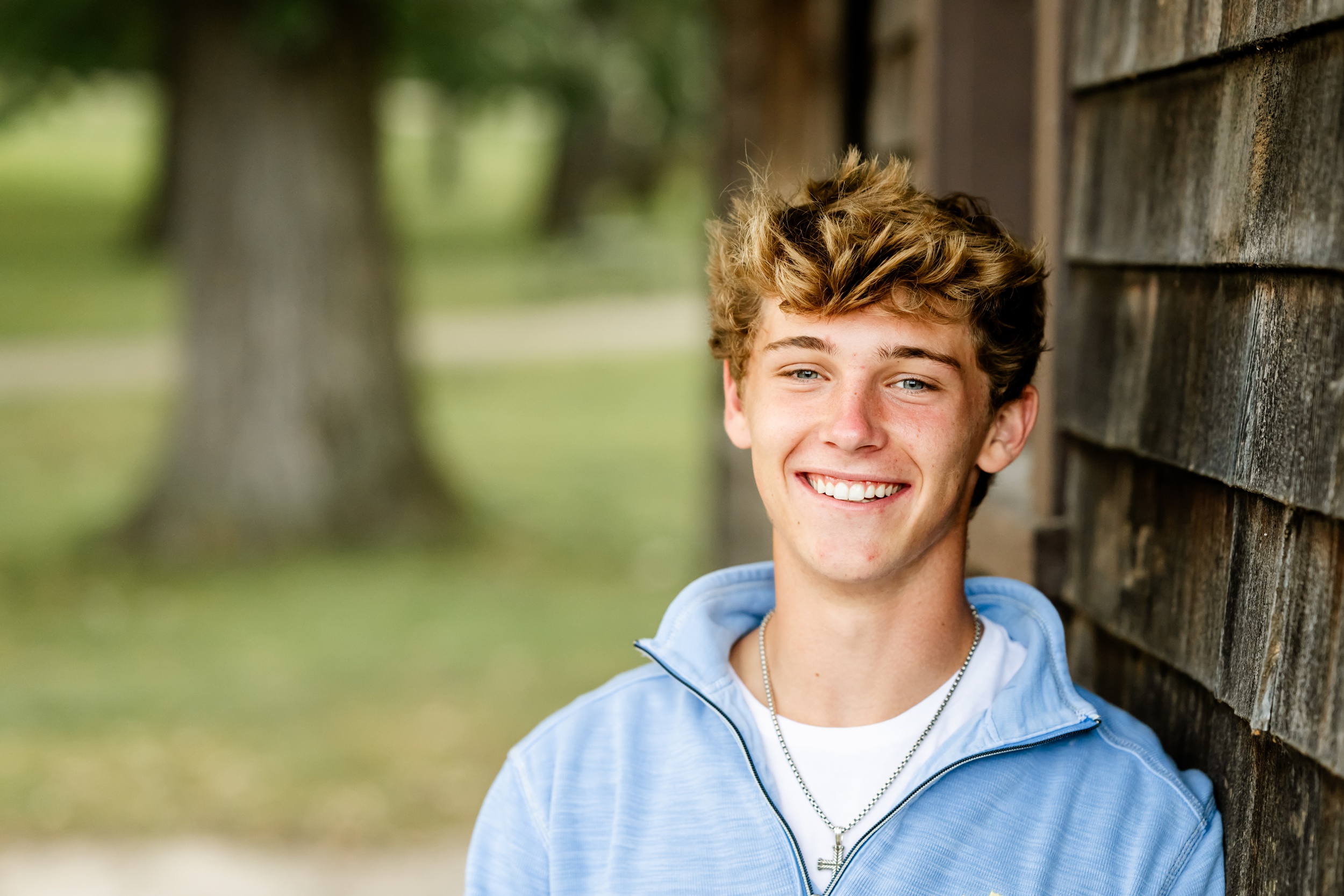 A closeup of a smiling teenager in blue and white leaning on a rustic structure after visiting hair salons in chicago