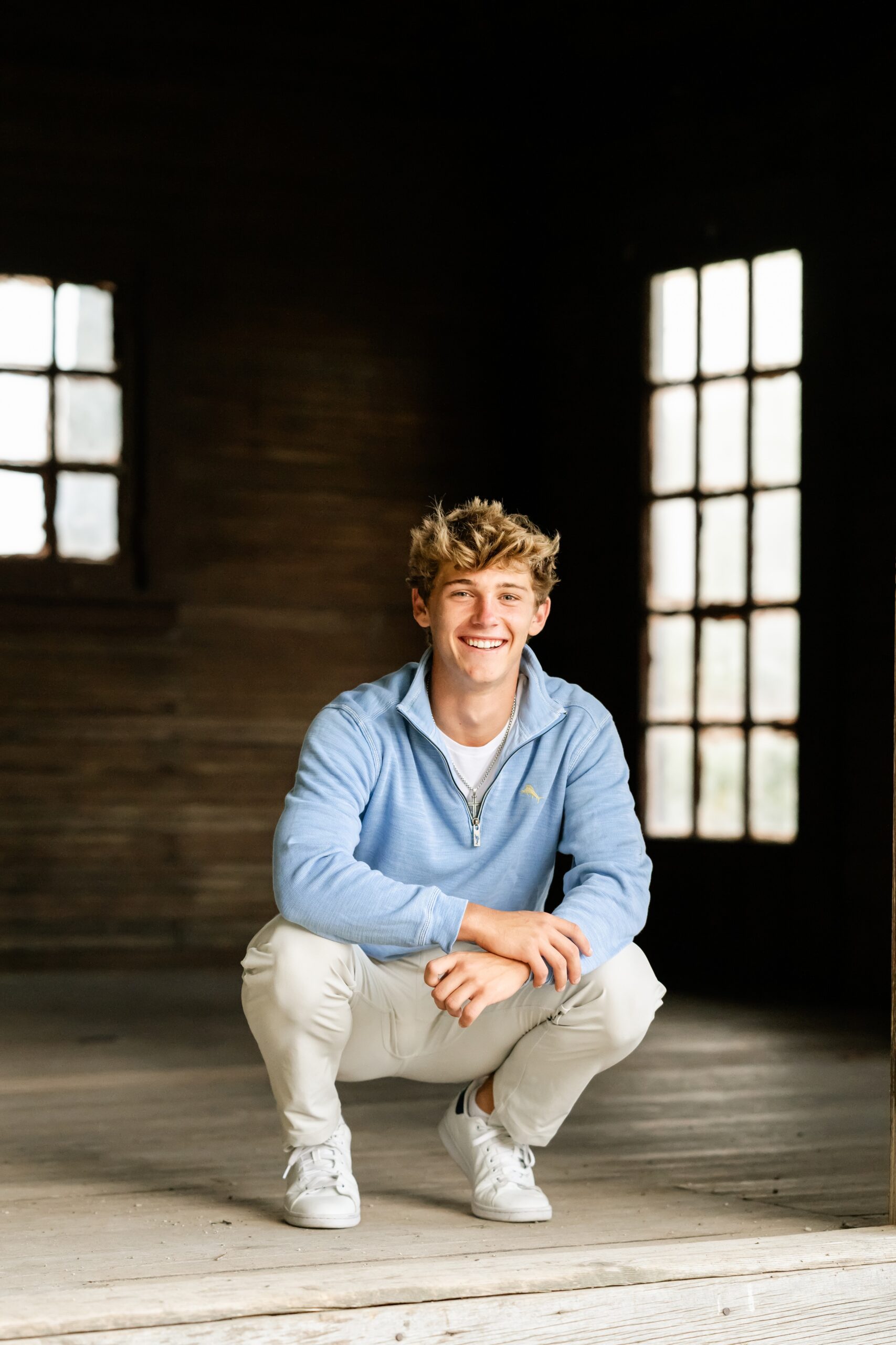 A teenager in a blue sweater squats in an old building while smiling after visiting hair salons in chicago