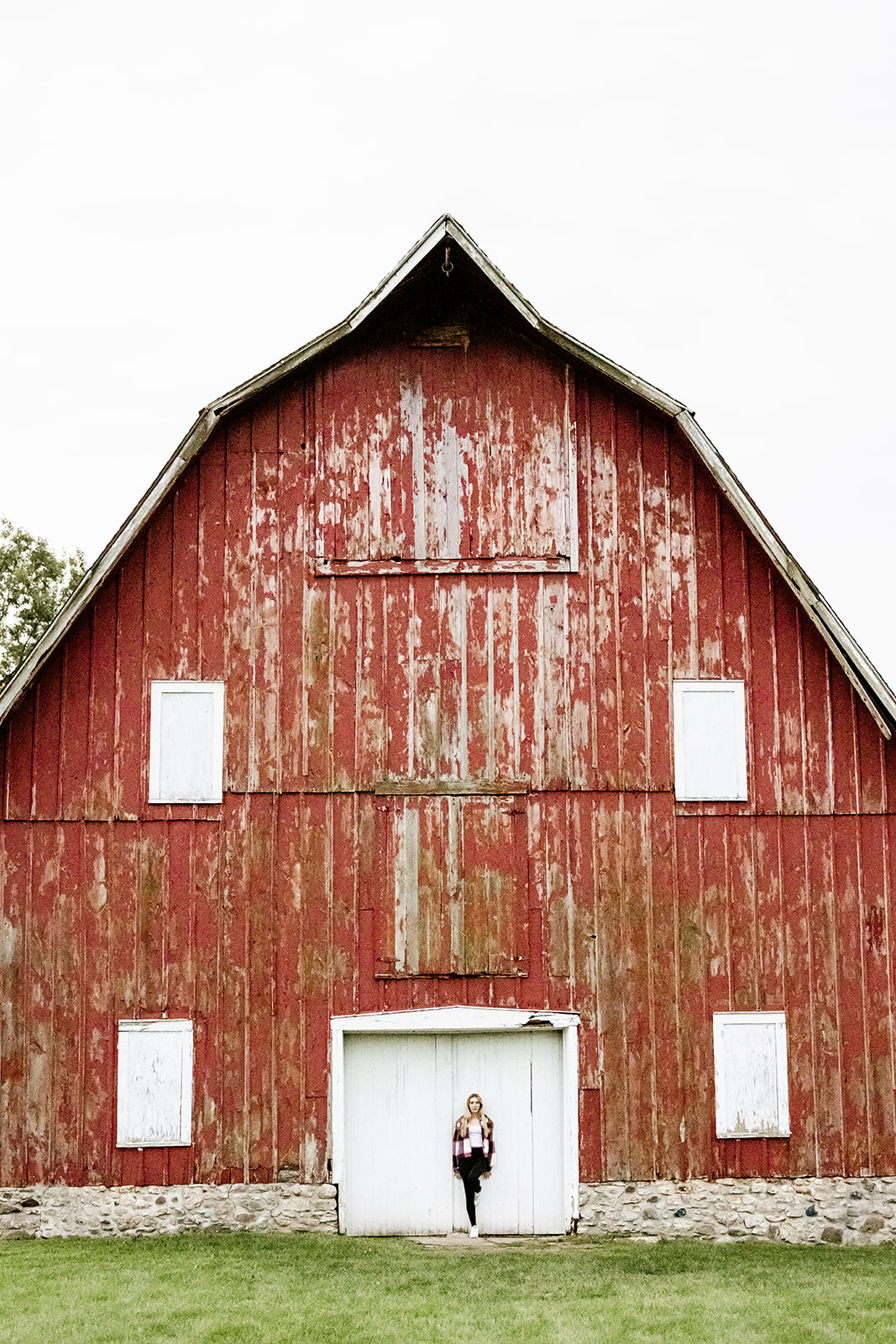 A teenager leans on the white doors of a large rustic red barn after visiting nail salons in Chicago