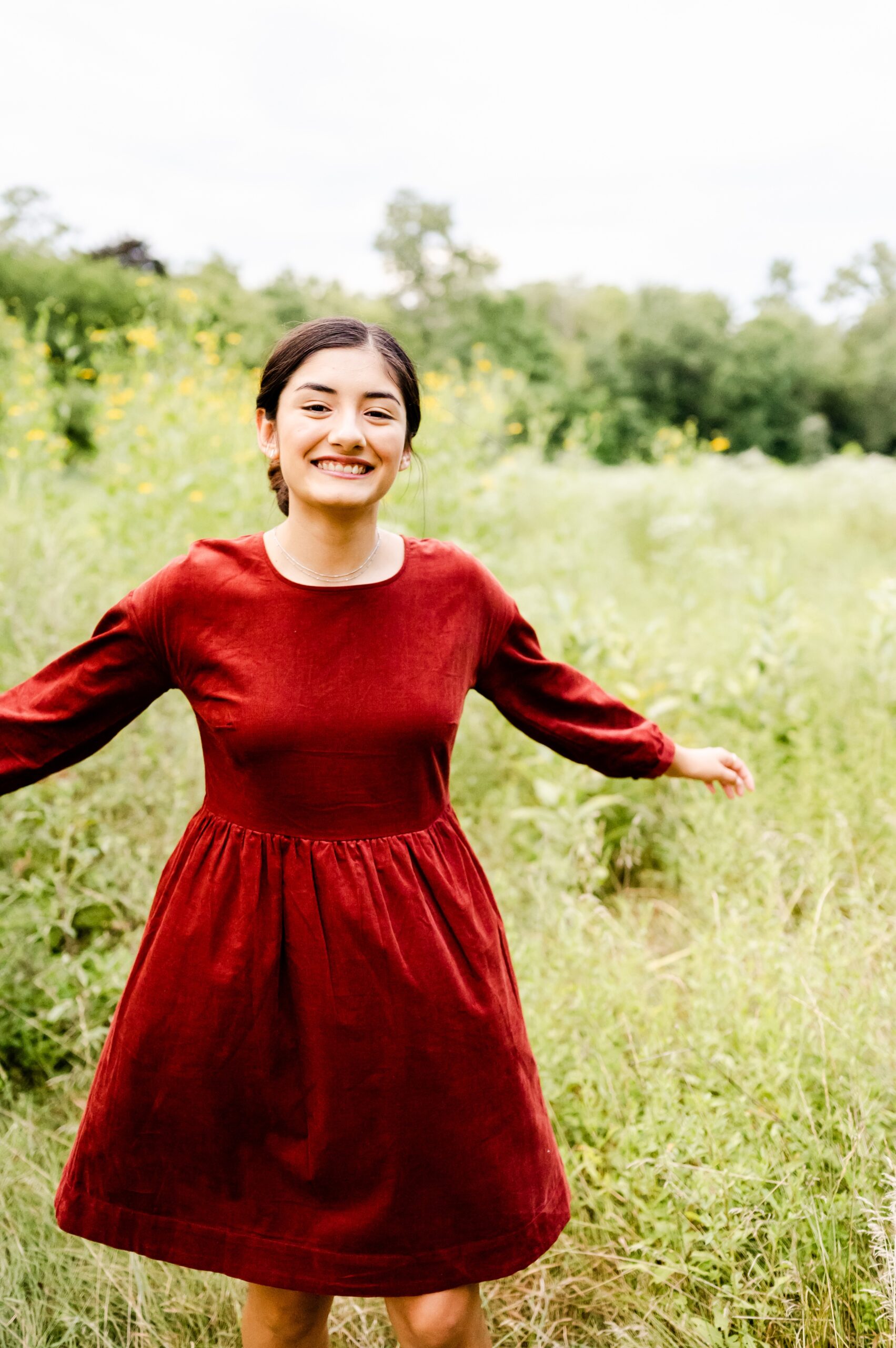 A happy woman in a red dress dances in a meadow of tall grass with a big smile
