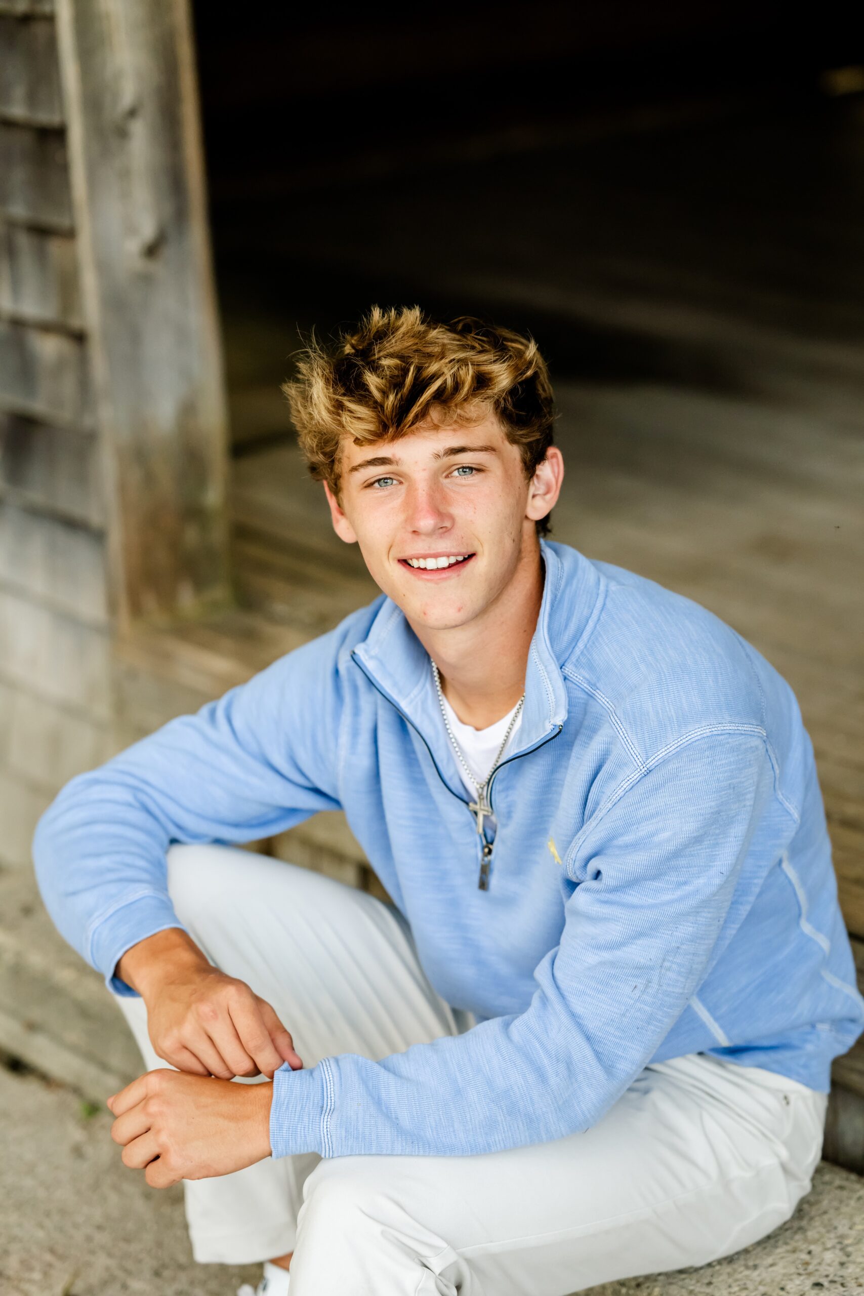 A teenager in a blue sweater sits on the steps of a rustic building in a park smiling after attending private high schools in Chicago