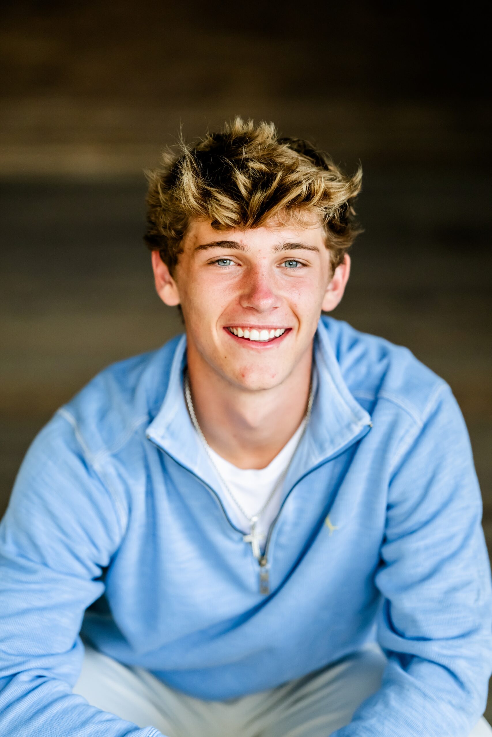 A happy teenager in a blue sweater smiles while leaning on his knees after visiting private high schools in Chicago