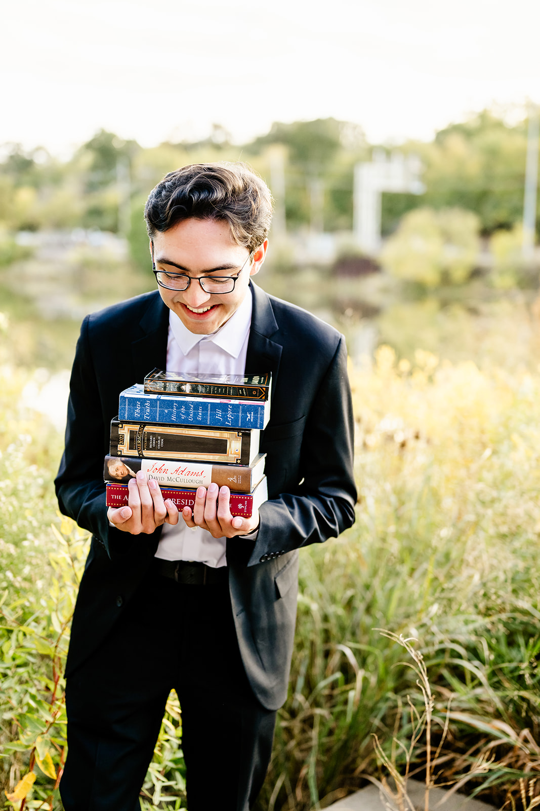 A laughing teenager carries a stack of books in a park