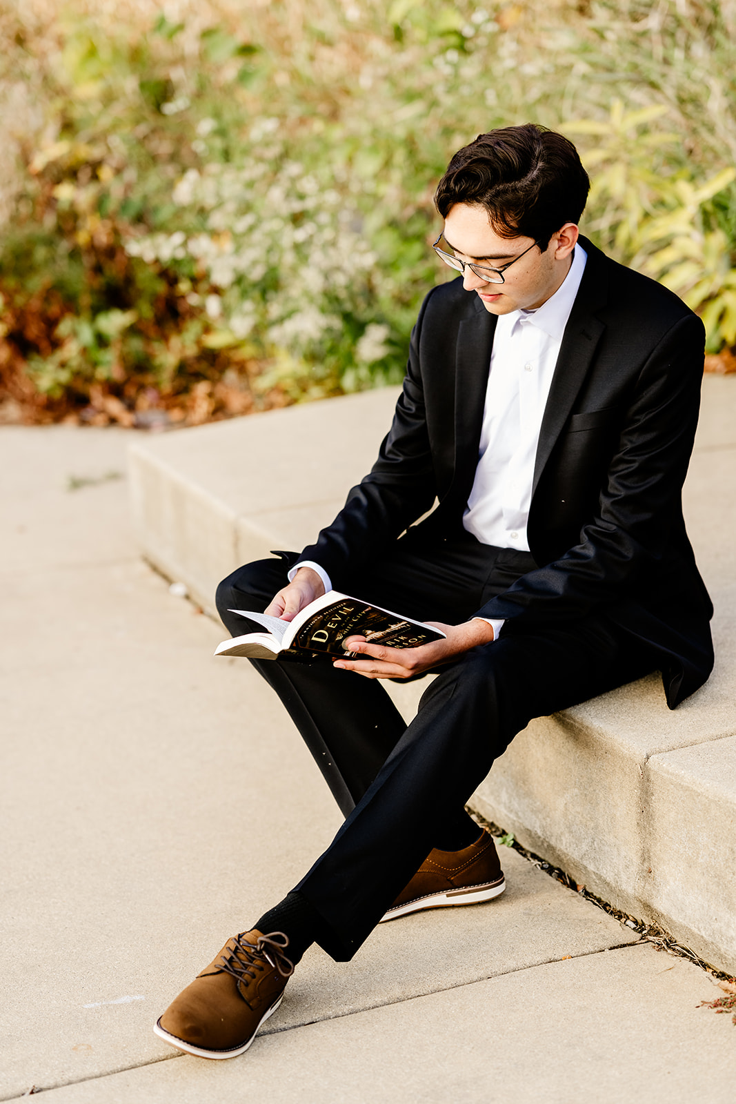 A high school senior sits and reads a book in a park after finding SAT prep in Chicago in a black suit jacket and slacks