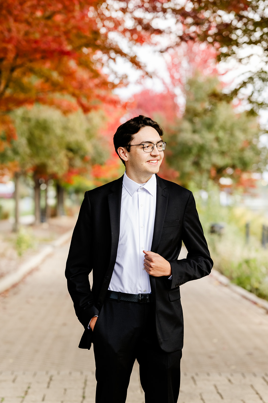 A happy teenager holds his black lapel while standing on a brick paved sidewalk