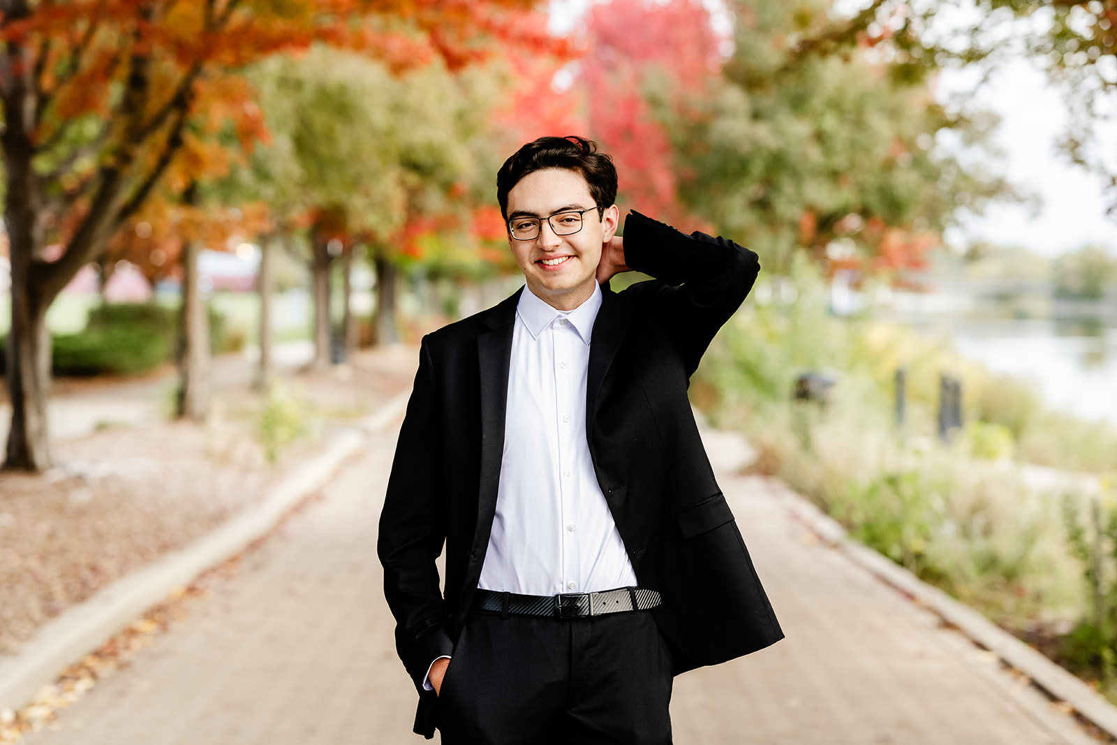 A happy high school senior in black jacket and slacks walks in a park in fall on a sidewalk after finding tutors in Naperville