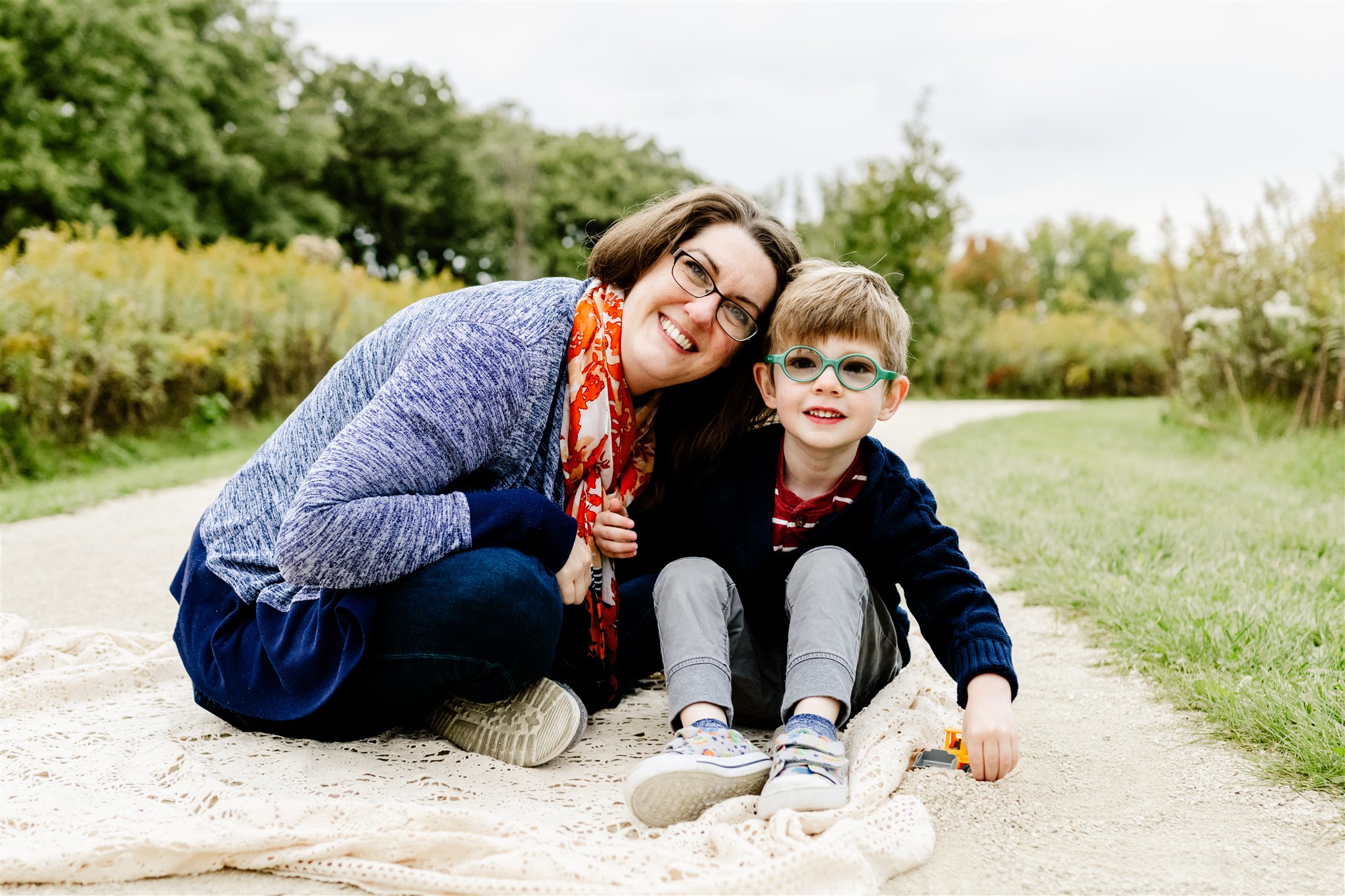 A toddler boy in a blue sweater plays with toys in a sandy path with happy mom after visiting Children's Museums in Chicago