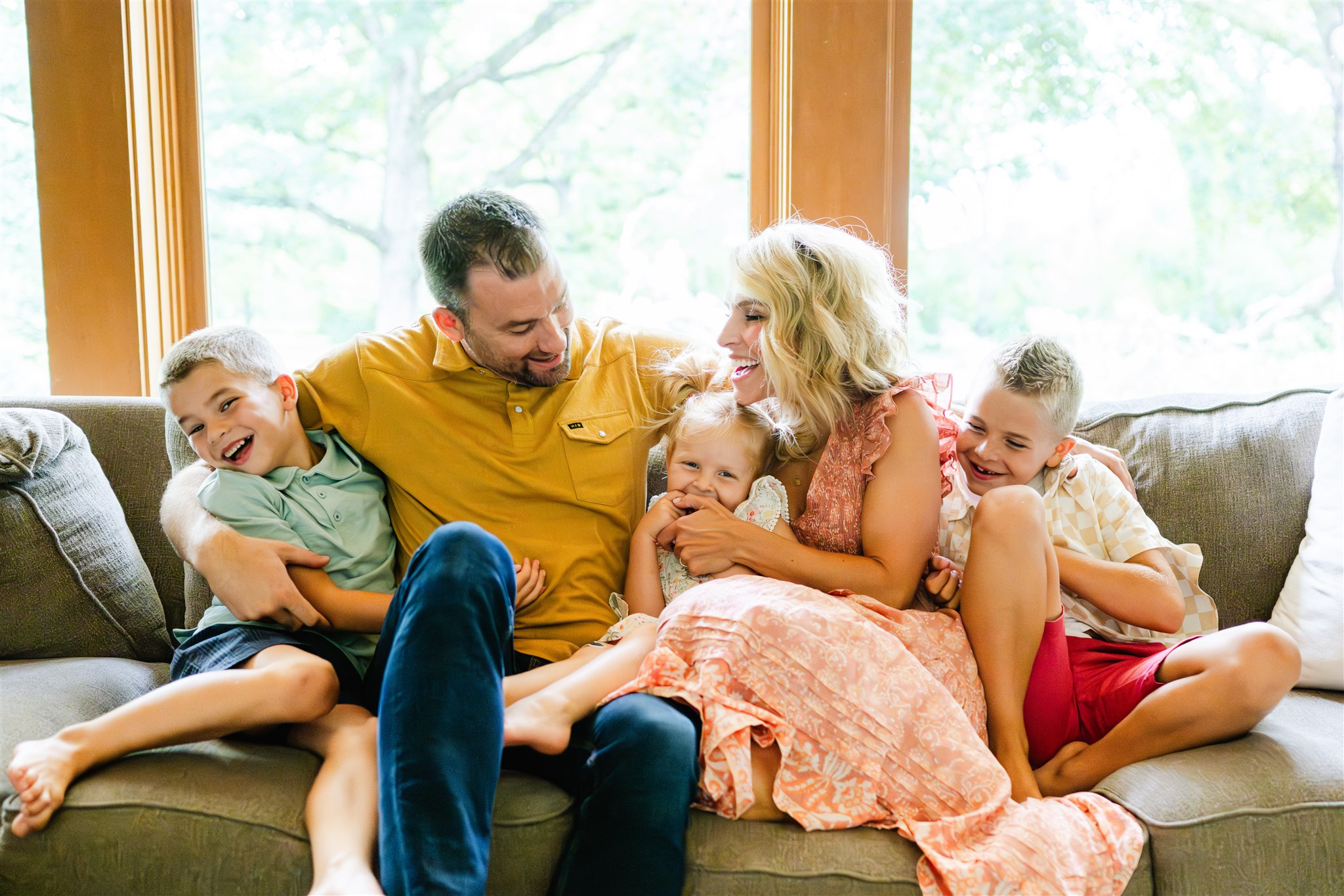 a happy family of five in colorful outfits laugh and play on a couch under windows after some family counseling in naperville