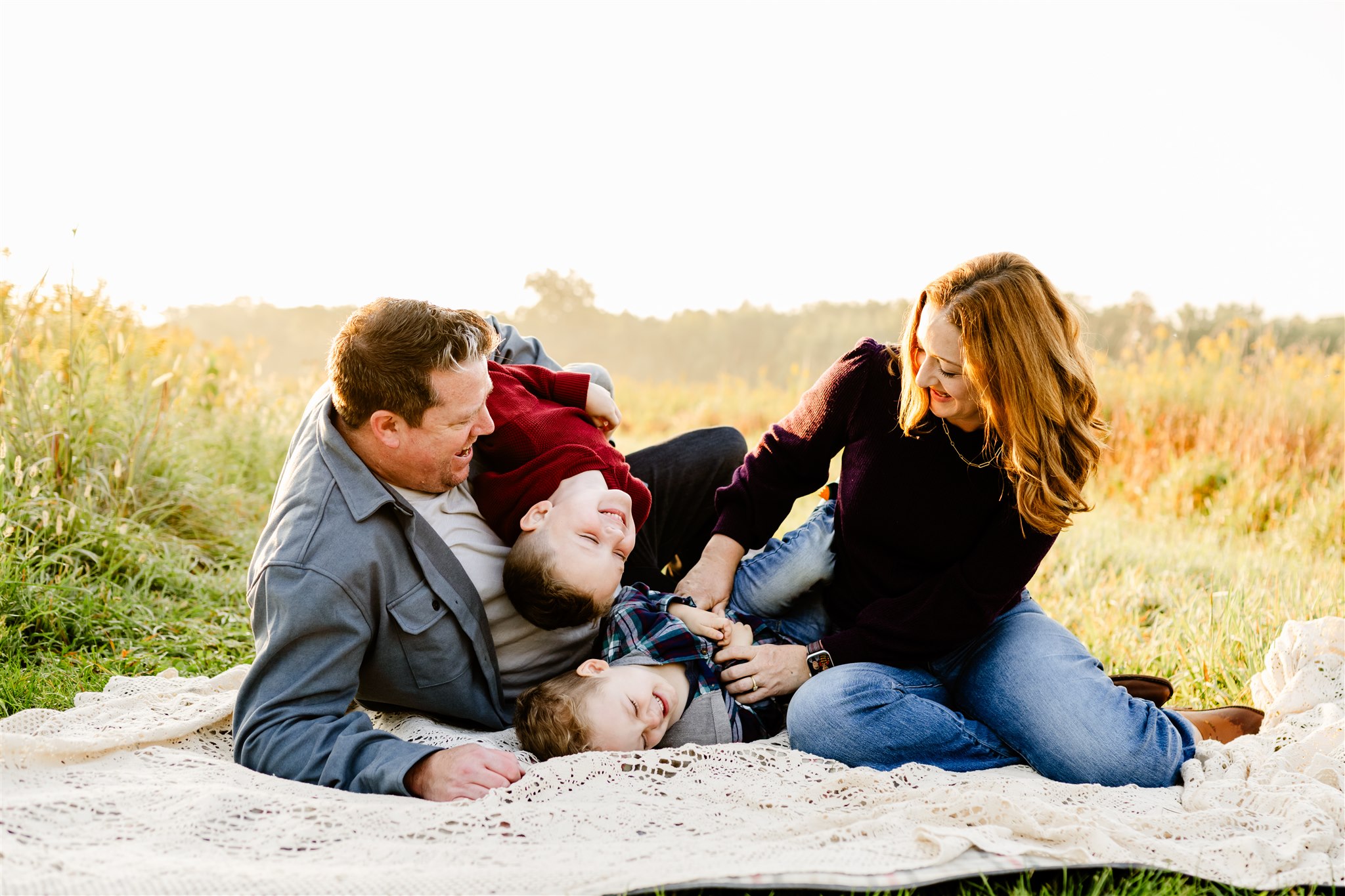 a mom and dad tickle and play with their two toddler sons on a picnic blanket in a a field of tall grass after some mommy and me classes in Chicago