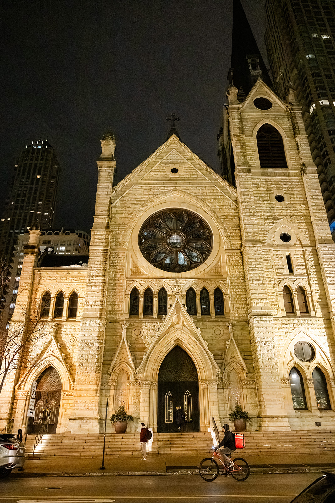 A look at the front facade of a Cathedral in Chicago as people walk or ride by