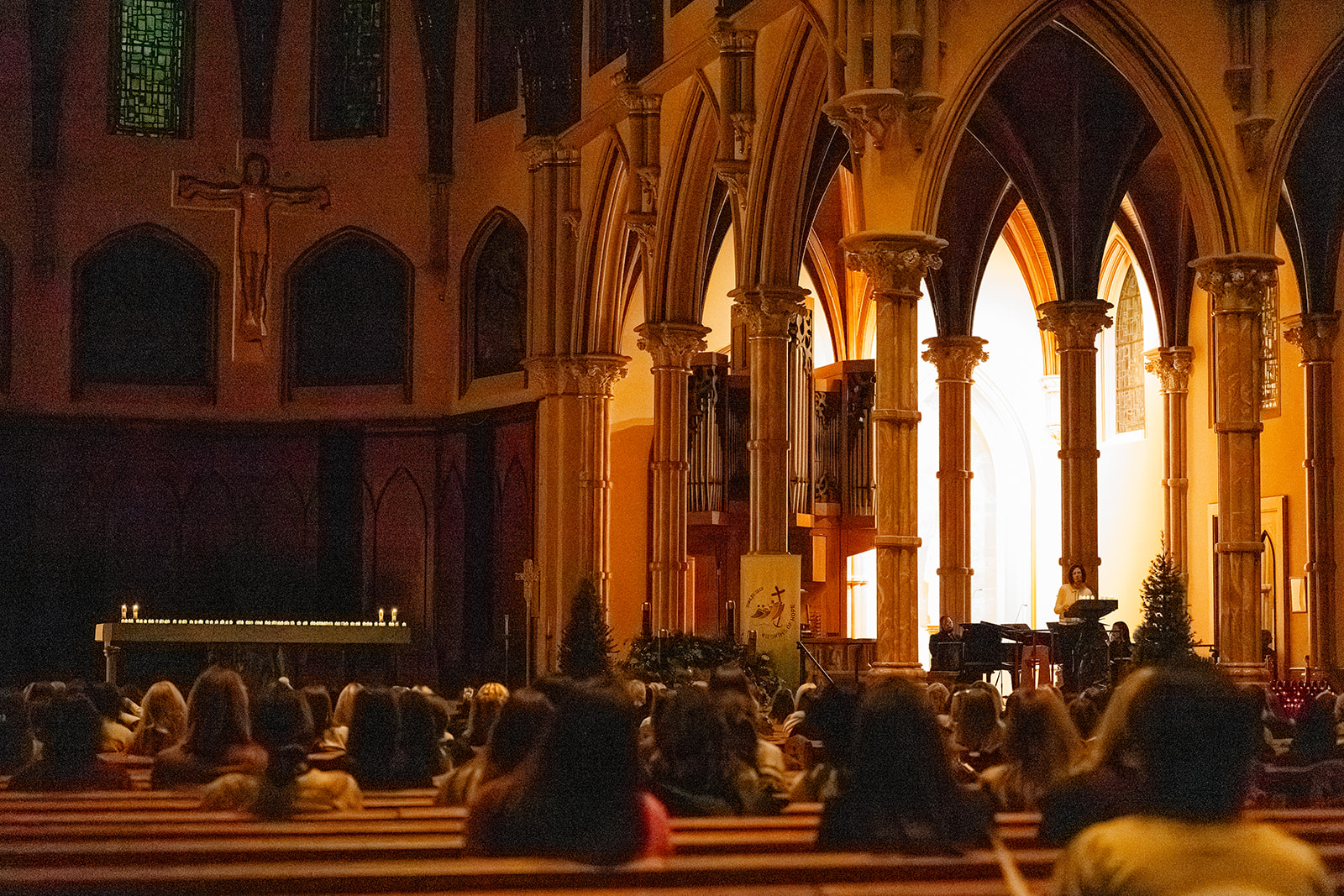 A woman stands at the ambo speaking or reading as women listen in in the pews during an Advent By Candlelight service
