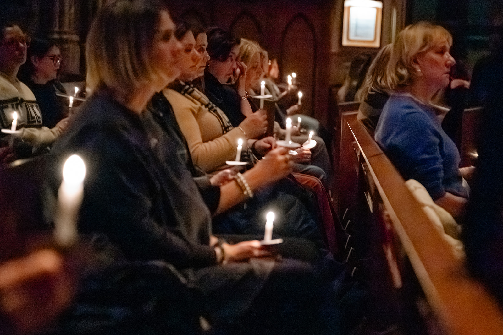 Women sit in a pew holding burning candles during an Advent By Candlelight service