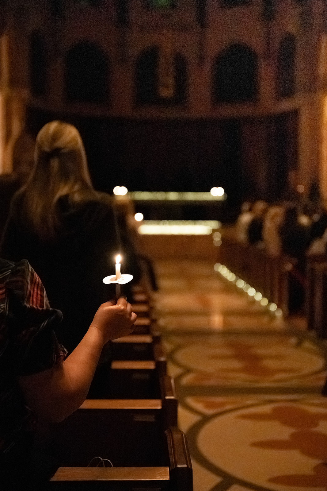 Details of a woman standing by the aisle holding a burning candle in a catholic church