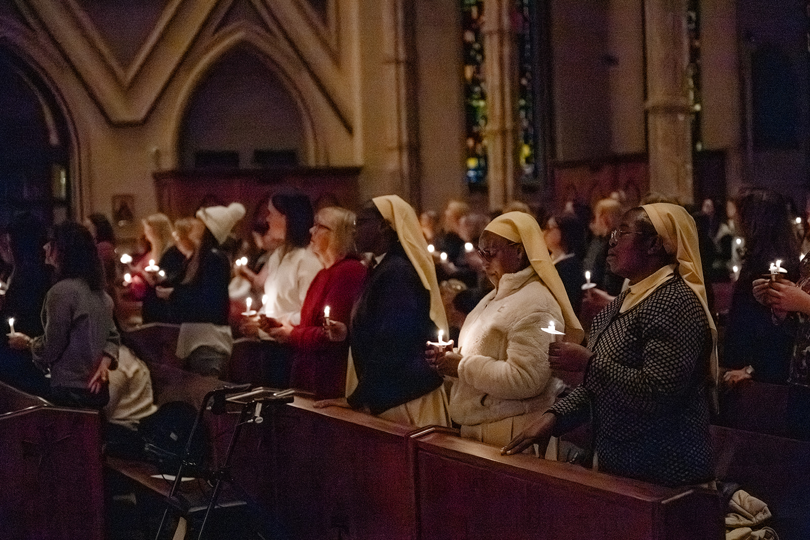 Women stand in a pews holding candles in a cathedral during an Advent By Candlelight service