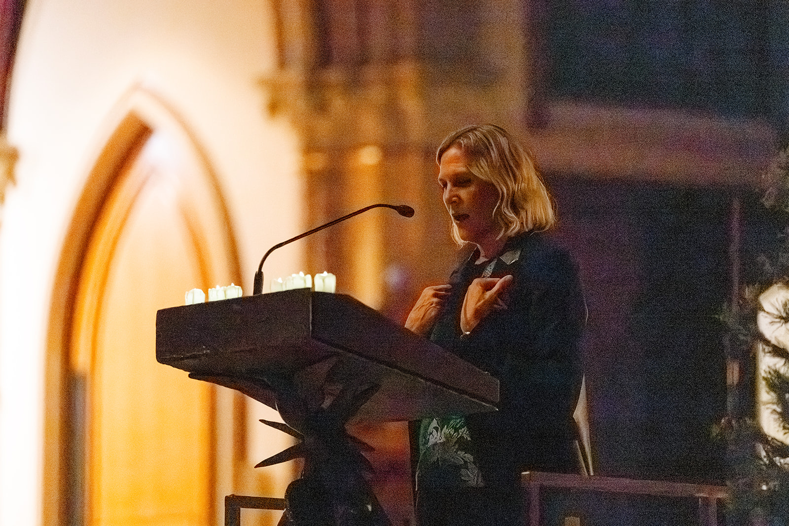 A woman reads at the Ambo in a black sweater with candles during Advent By Candlelight