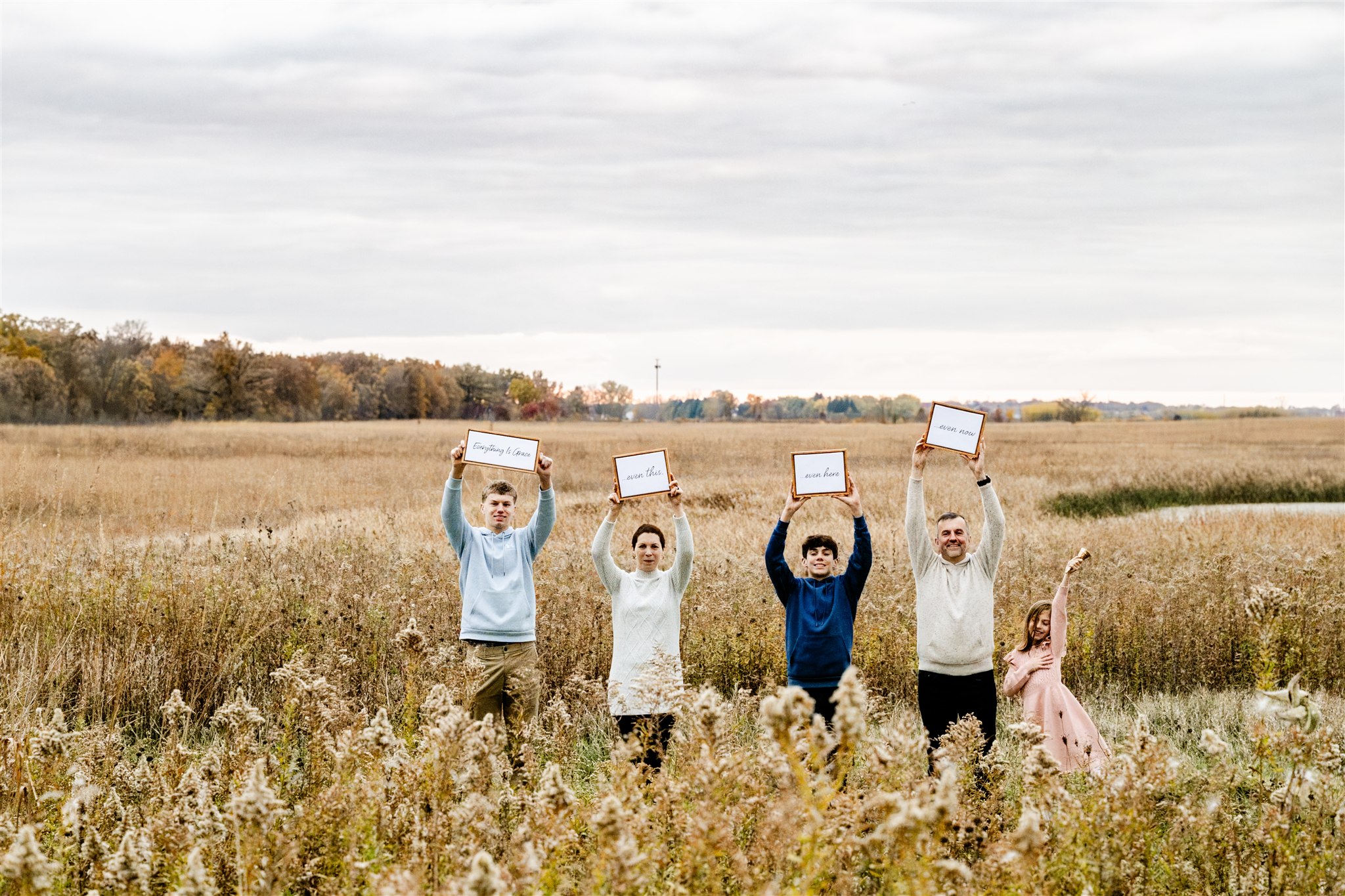 A family of five stand in a field of tall grass holding signs above their heads after leaving Cancer Support Center in Chicago