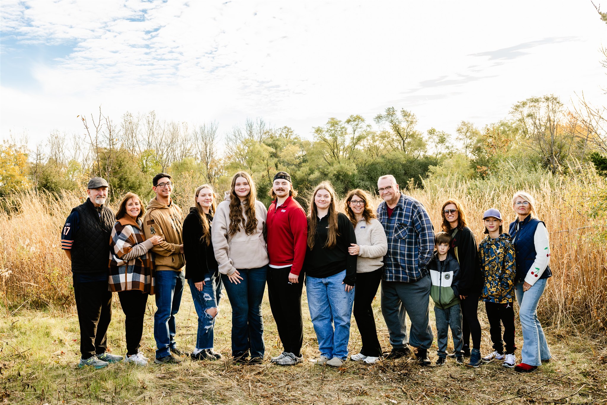A large extended family stands smiling in a park trail at sunset