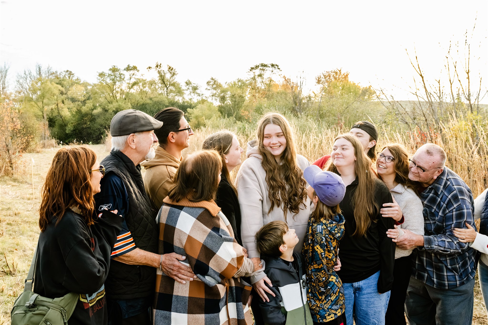 A teen girl cancer survivor smiles while surrounded by her large extended family in a field at sunset thanks to Delnor Hospital Cancer Center