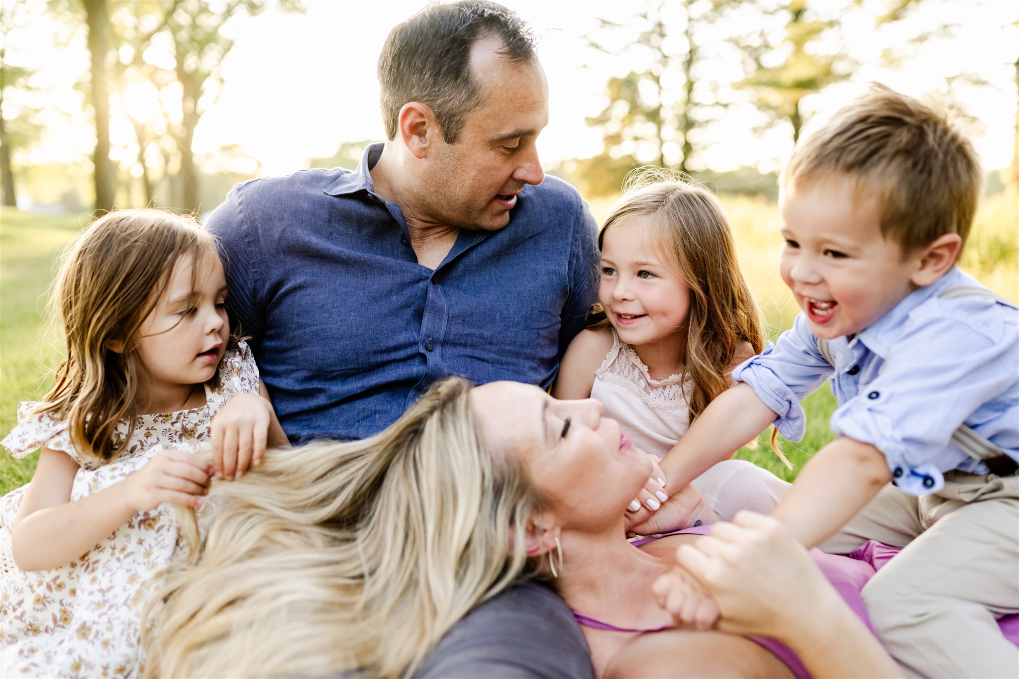 A mom and dad play in a park lawn with their three toddlers in their laps after some family counseling in Chicago