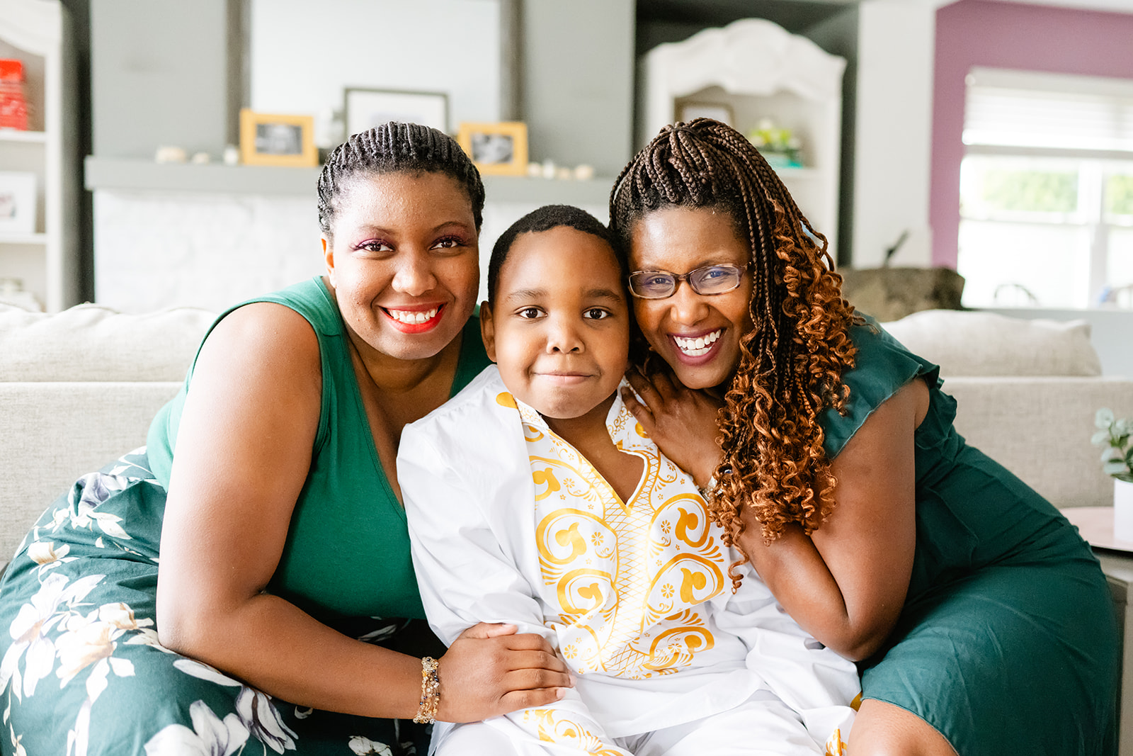 Smiling women in green hug onto their smiling son in a white and gold shirt on a couch
