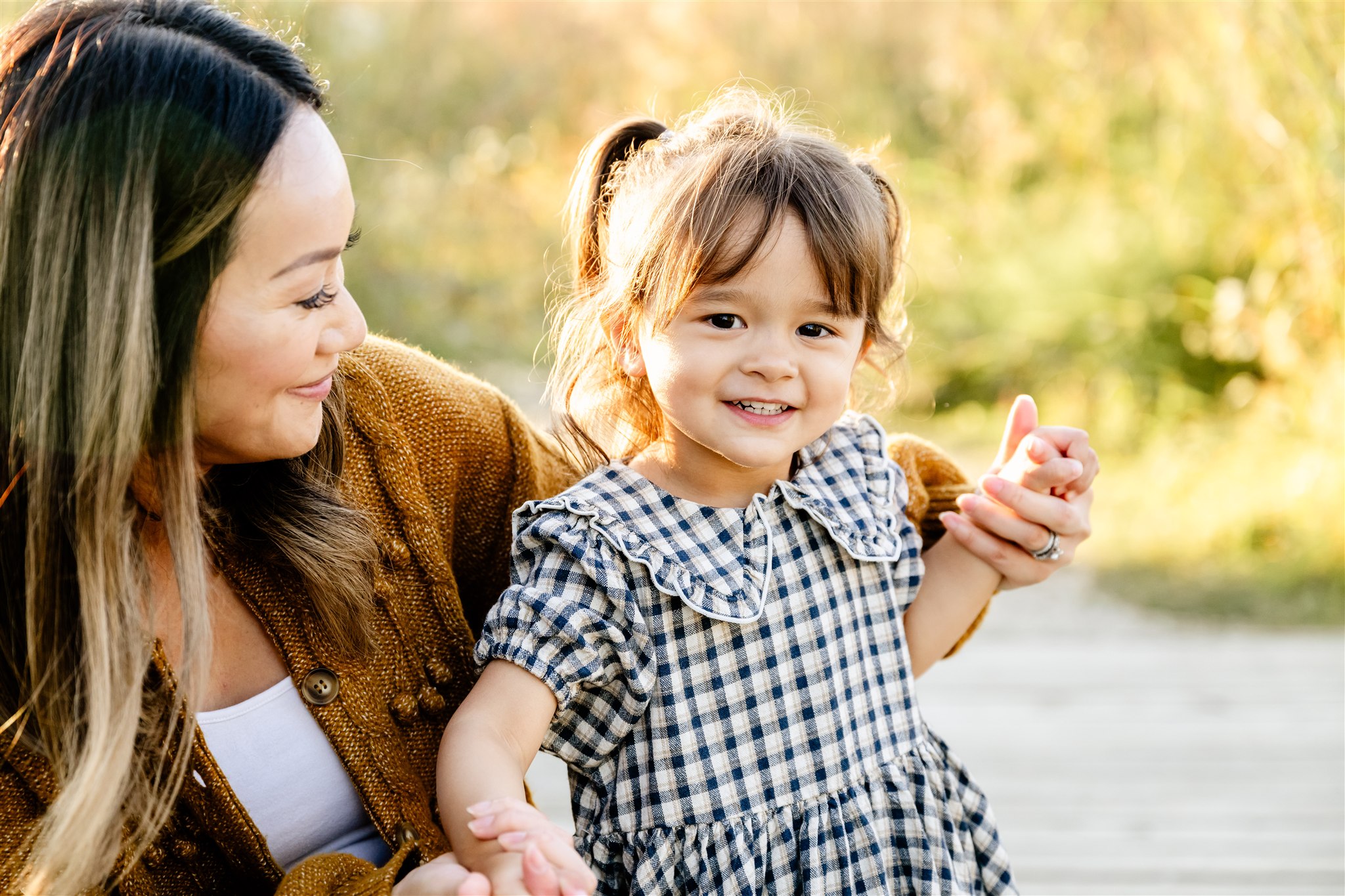 A happy toddler girl in a black and white dress smiles while walking a park with mom at sunset before visiting kid-friendly restaurants in Chicago