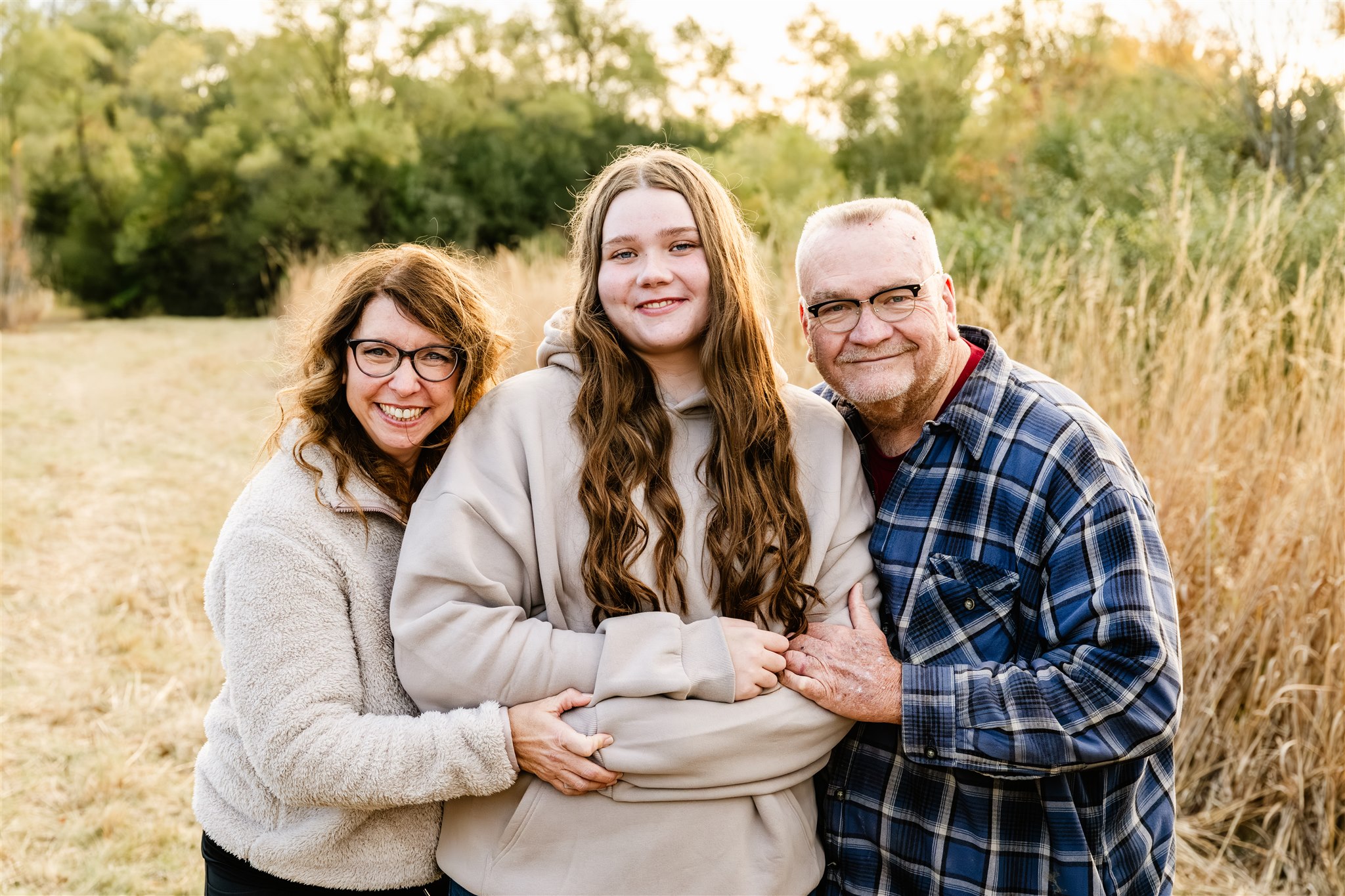 Smiling mom and dad stand in a park hugging onto their teen daughter in blue and tan sweaters thanks to Loyola Hospital Cancer Center