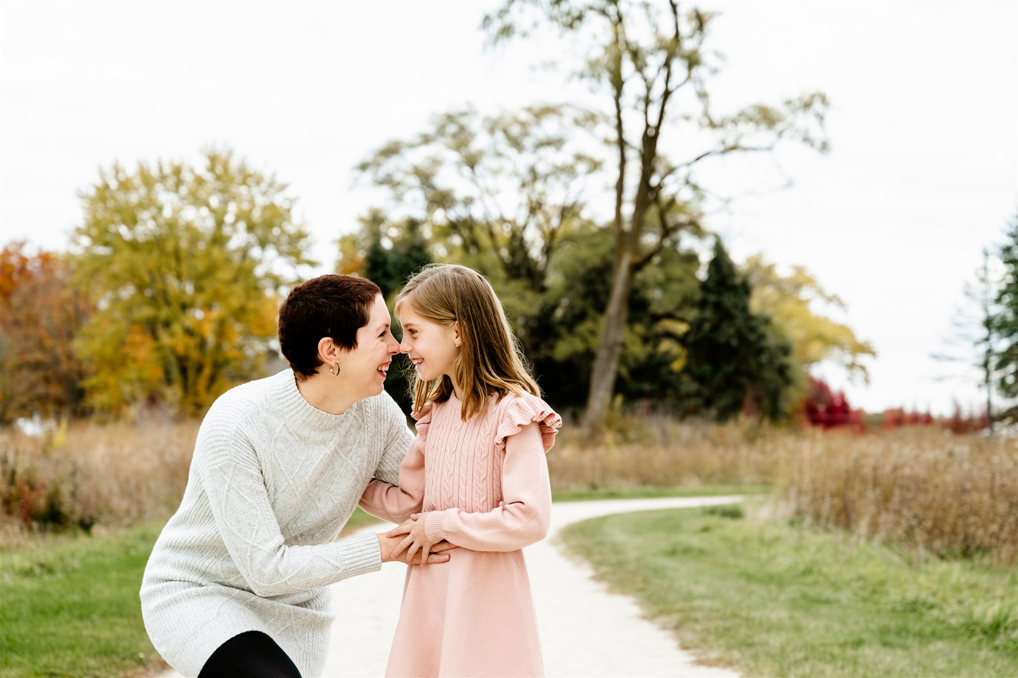 a smiling young girl boops noses with her mom in a white sweater on a park trail thanks to Wellness House in Hinsdale, IL