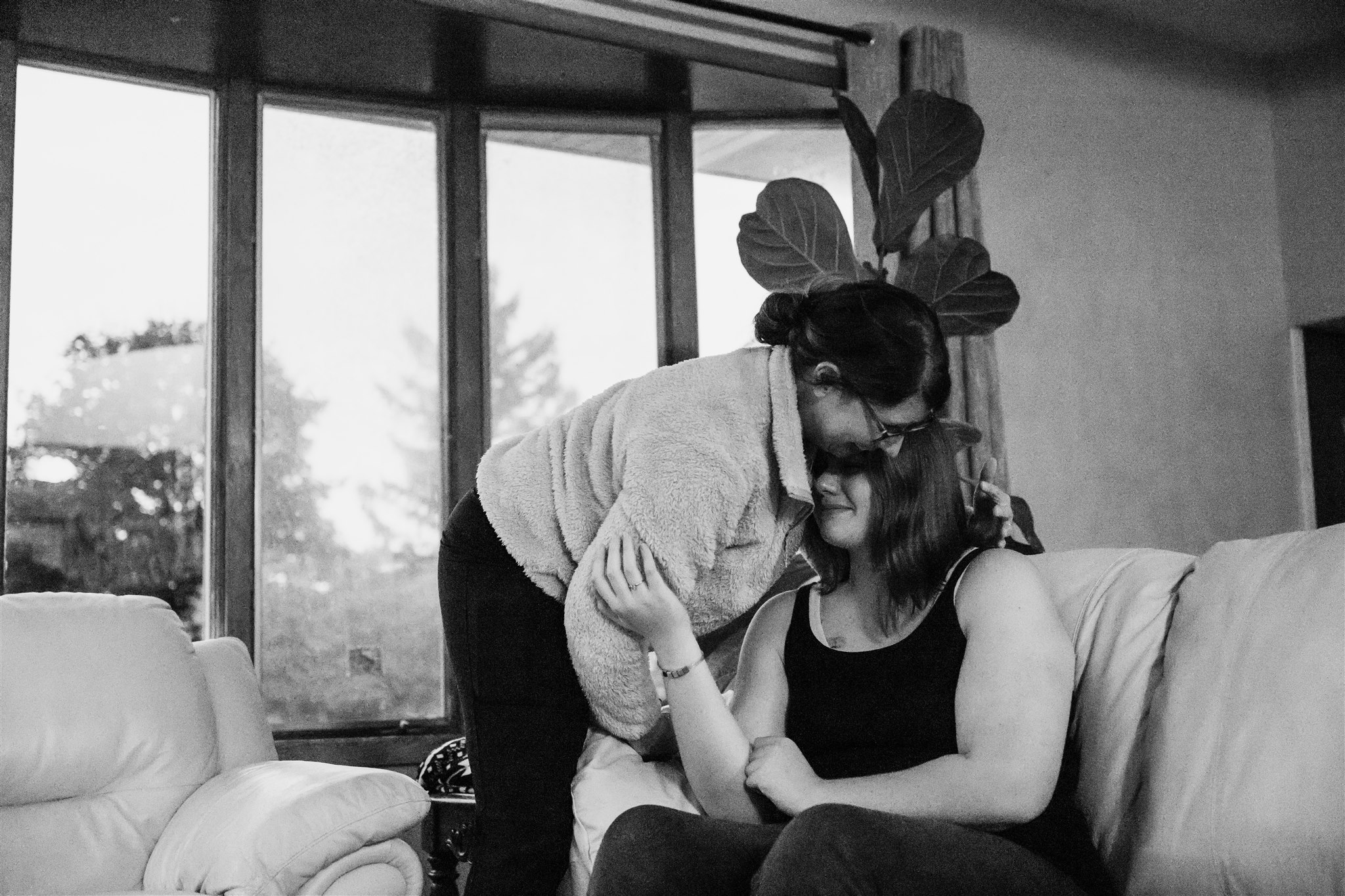 A mom hugs her daughter while sitting on a couch in a black top
